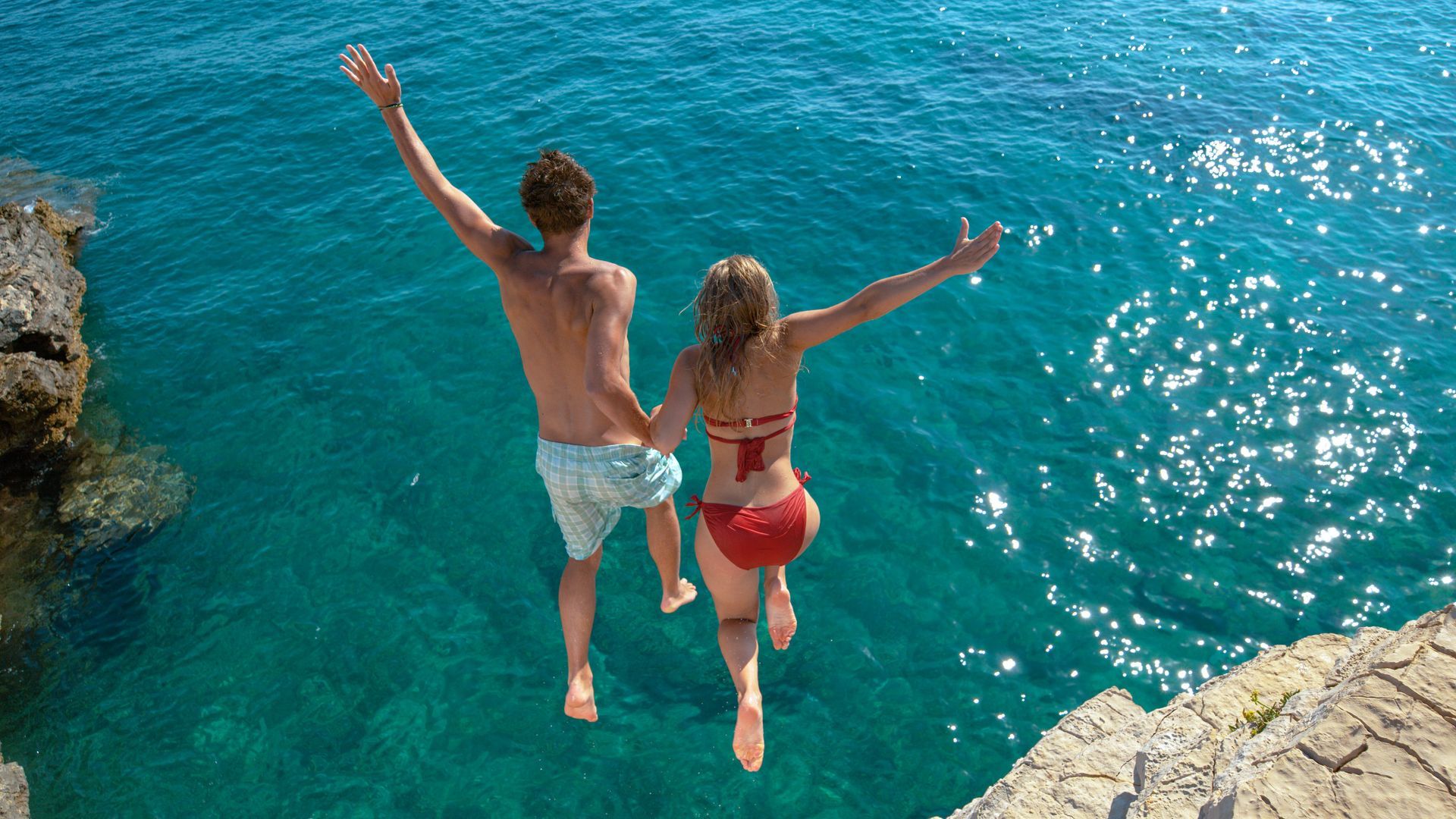 A man and a woman are jumping into the ocean from a cliff.