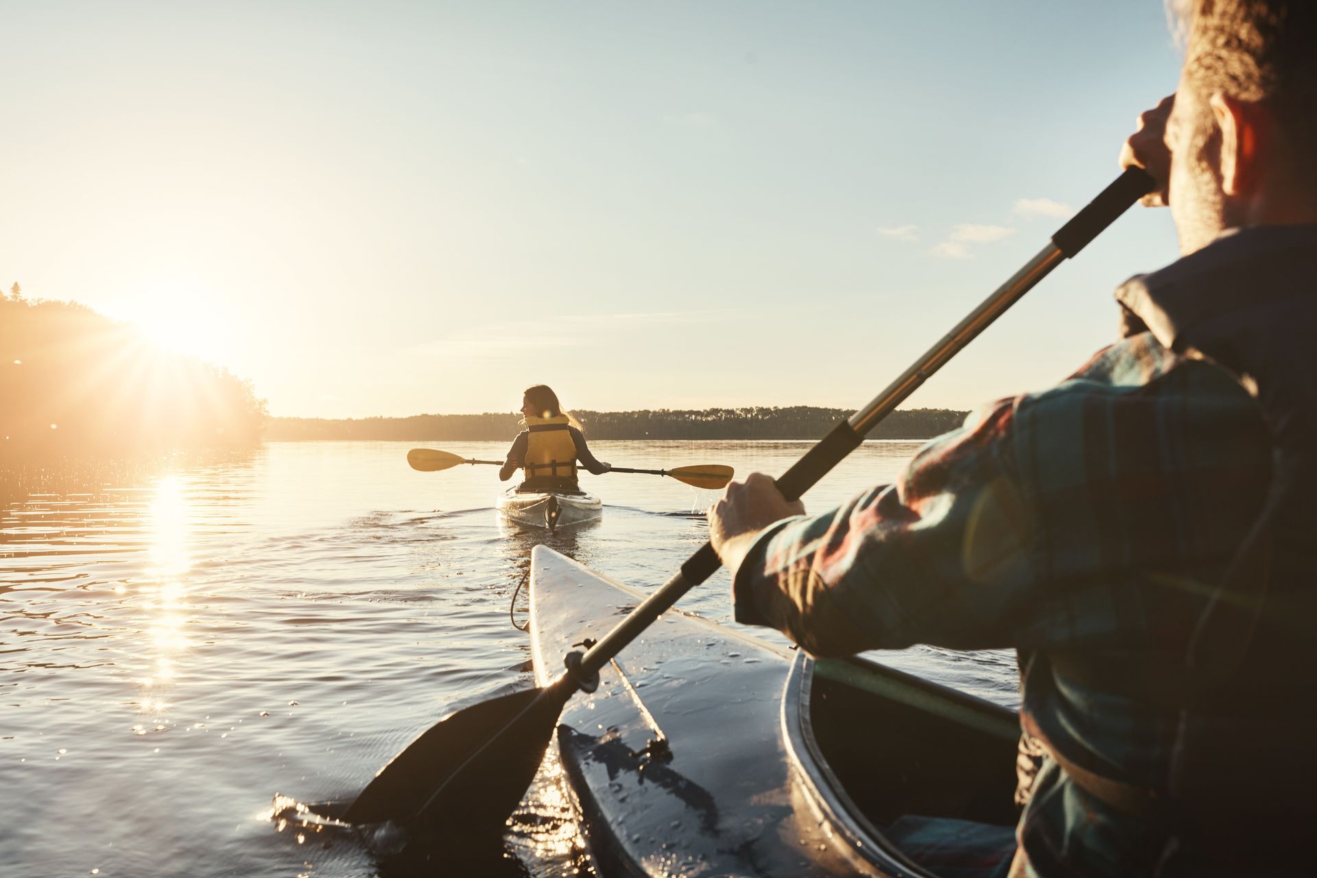 Kayakers on a lake at sunset, person in foreground paddling toward another.