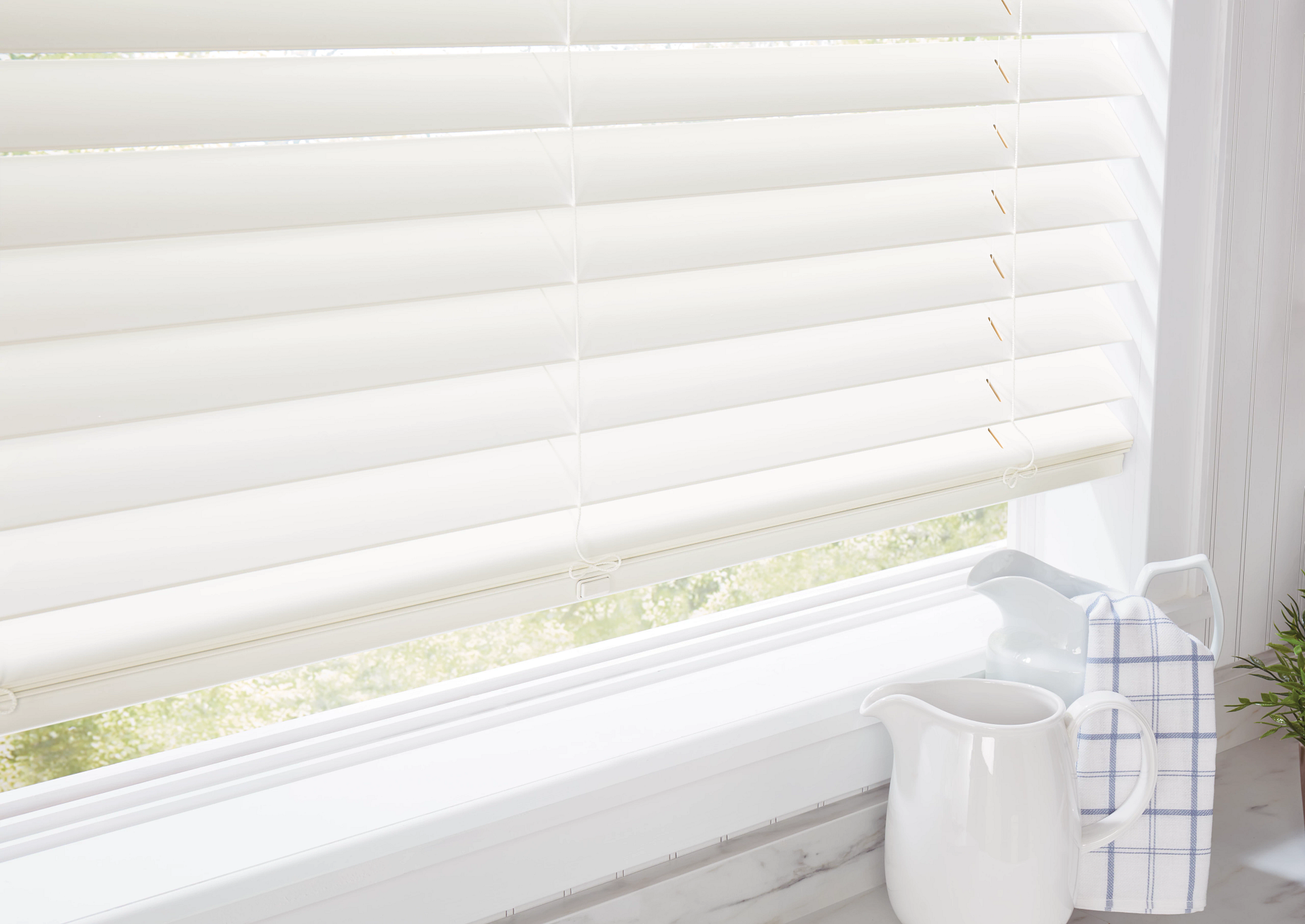 White window blinds above a windowsill with a small white pitcher and a blue-and-white jar