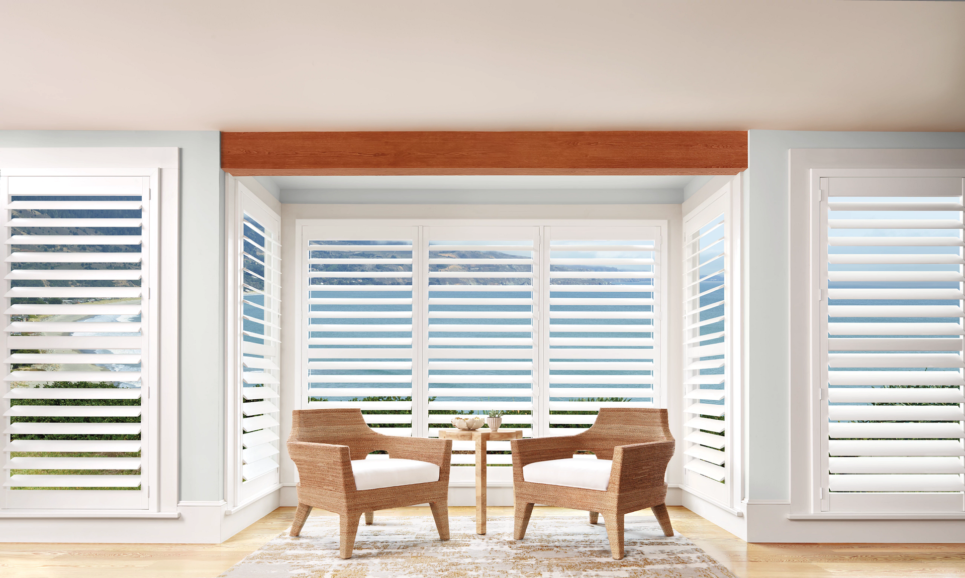 Bright sunroom with white blinds, two wicker chairs, and a small table on a light wood floor