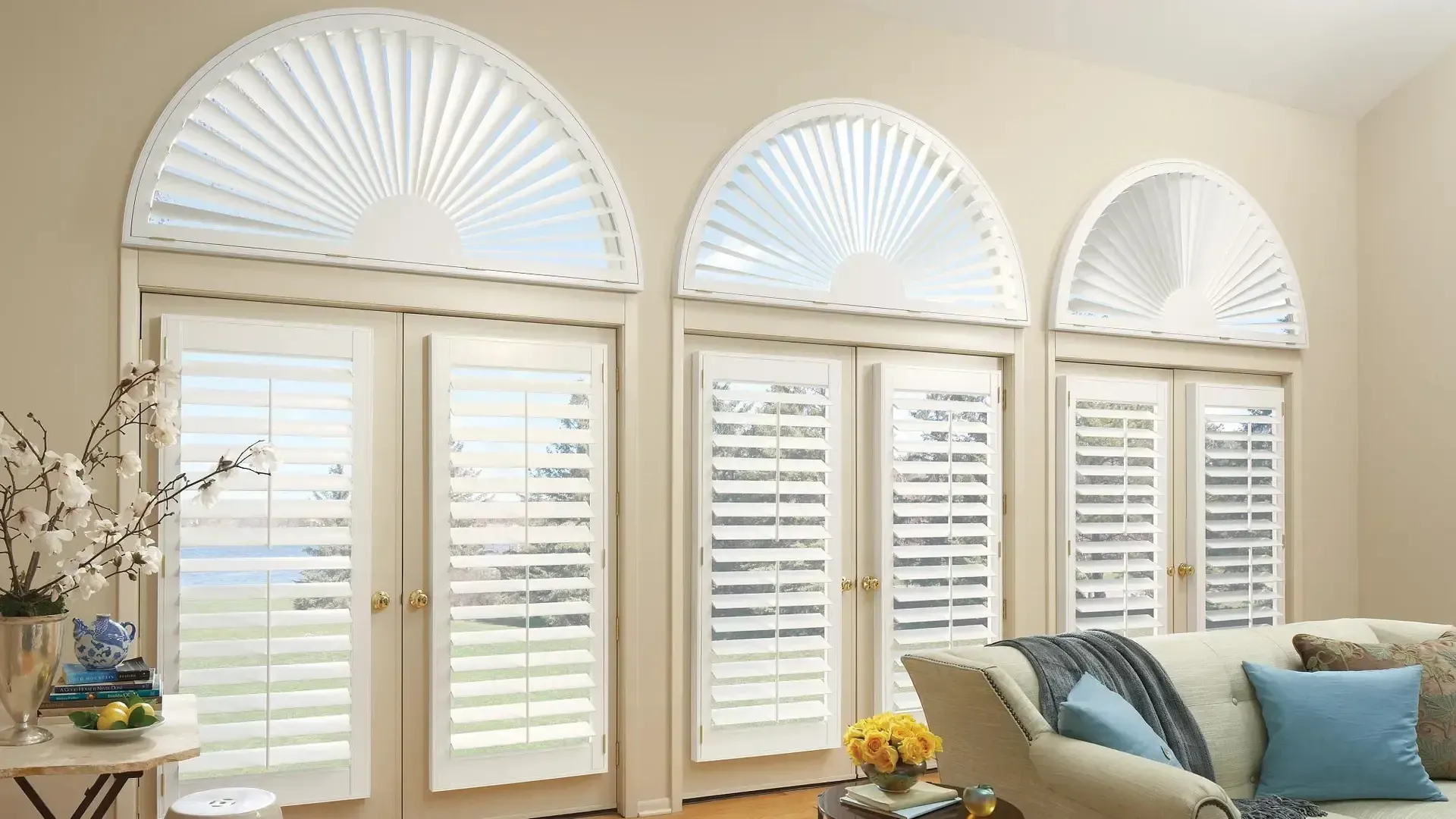 Bright living room with three arched windows, white shutters, and a sofa with blue pillows