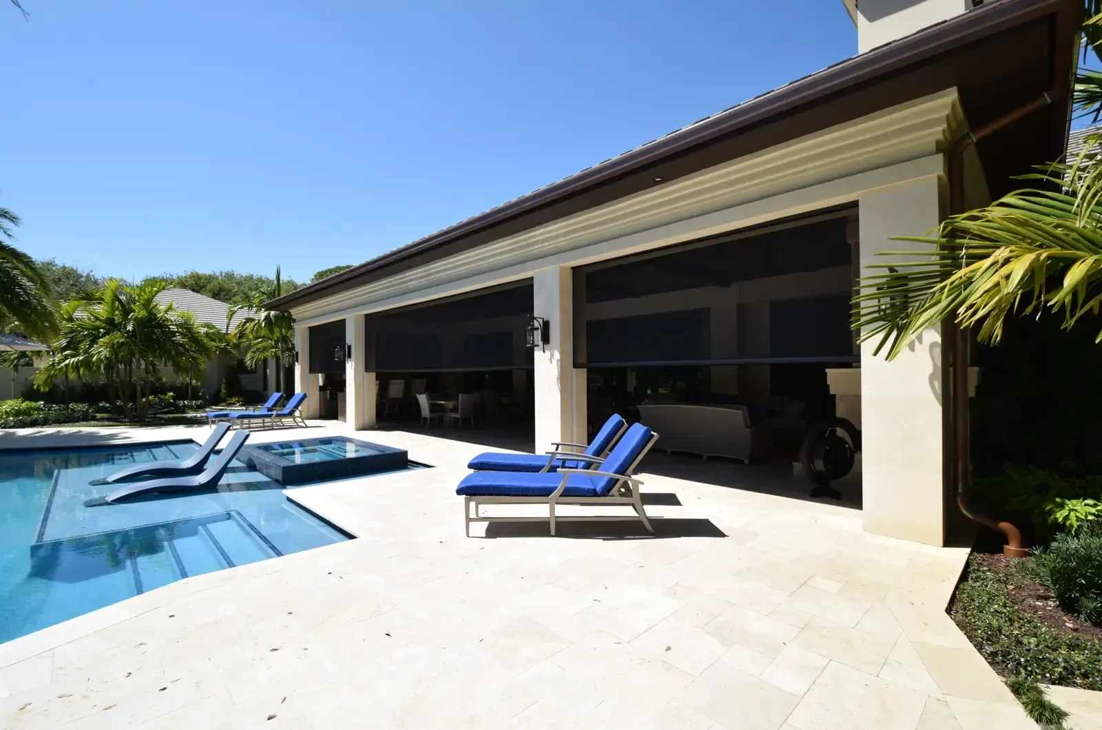 Modern patio with a pool, lounge chairs, and a covered outdoor living area under a sunny sky