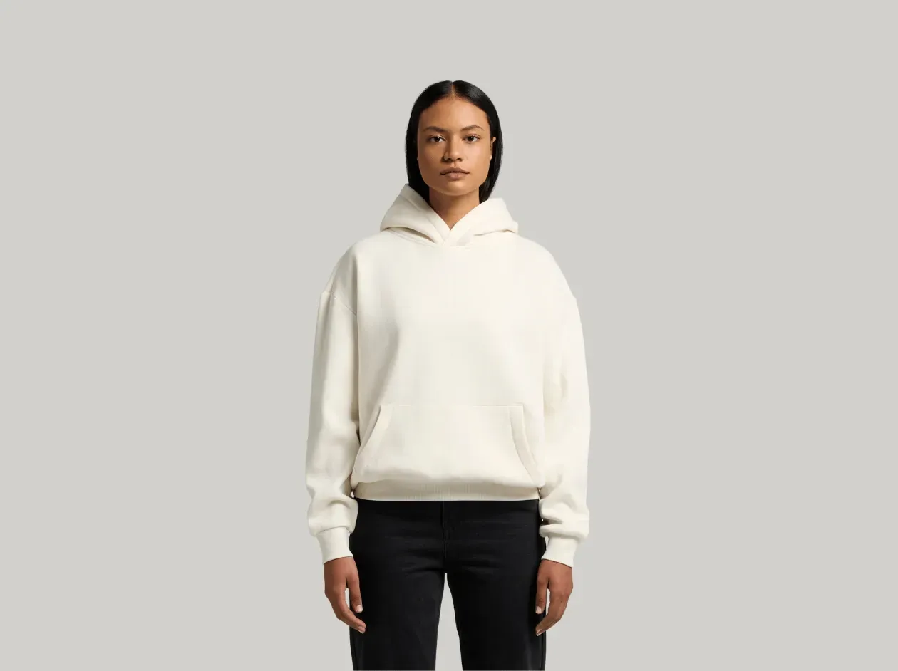 Person standing against a light gray background wearing a cream hoodie and black pants