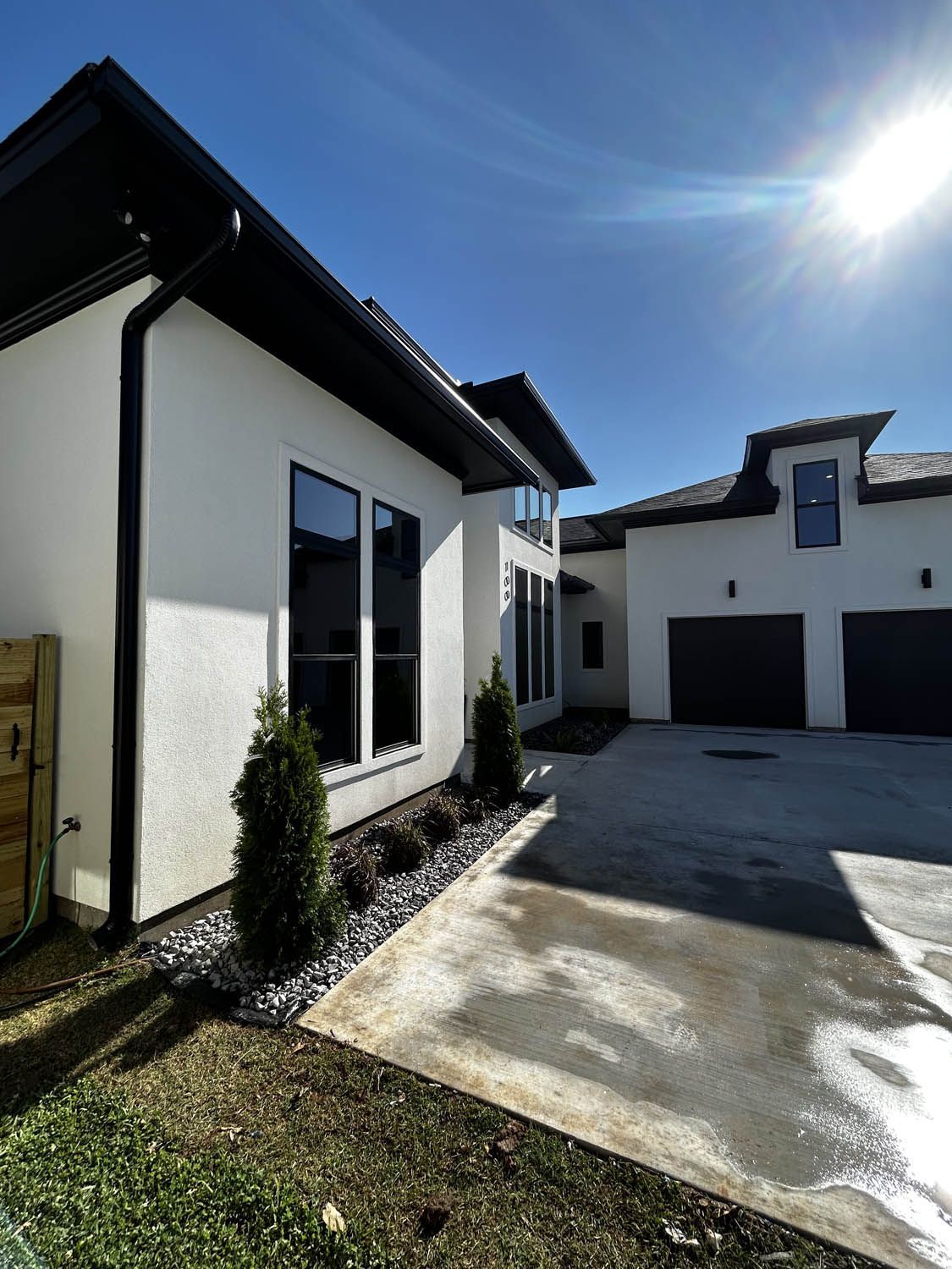 White stucco house with black trim, black garage doors, and a clear blue sky.