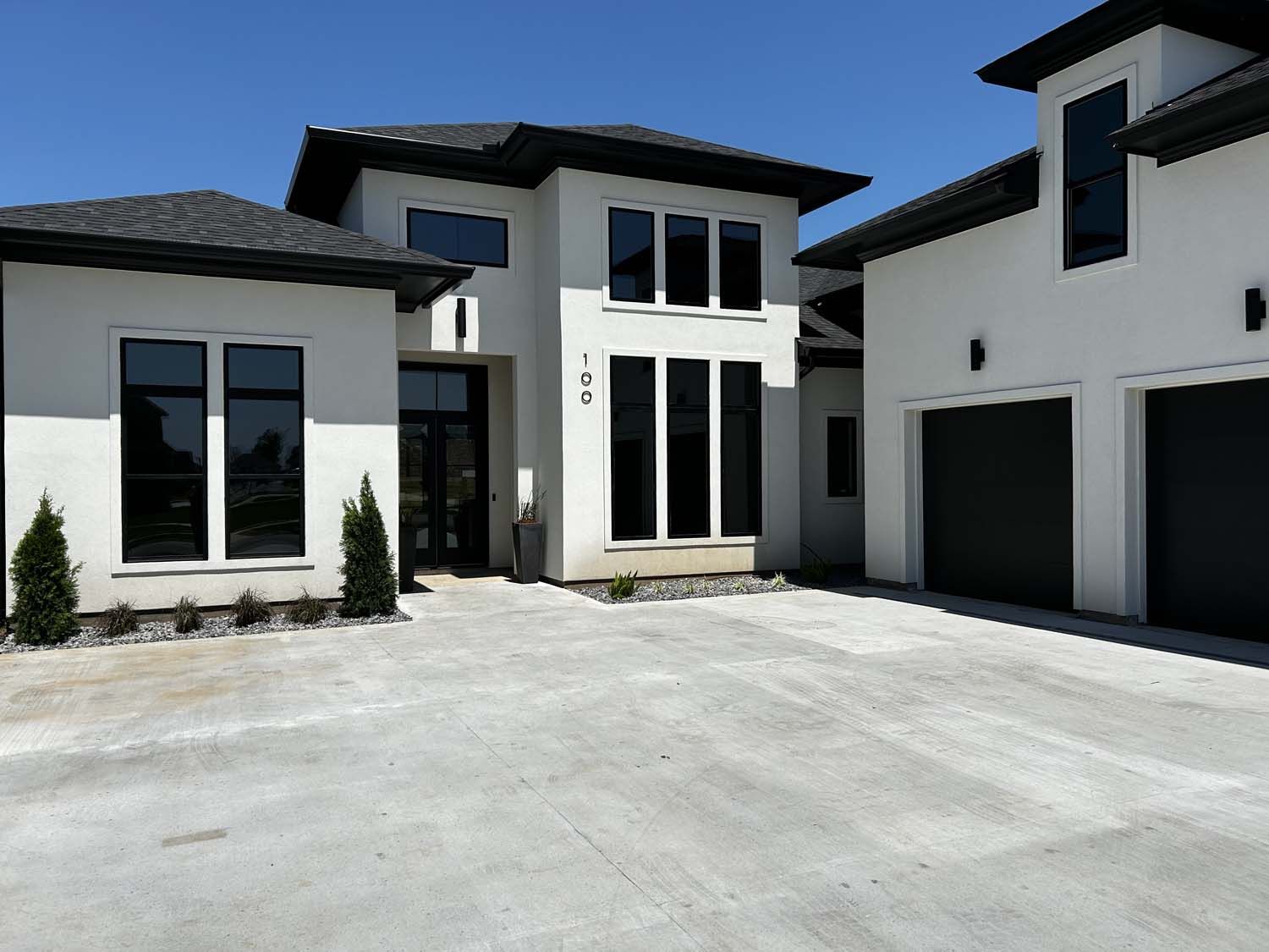 Modern white stucco house with black trim and garage doors, concrete driveway.