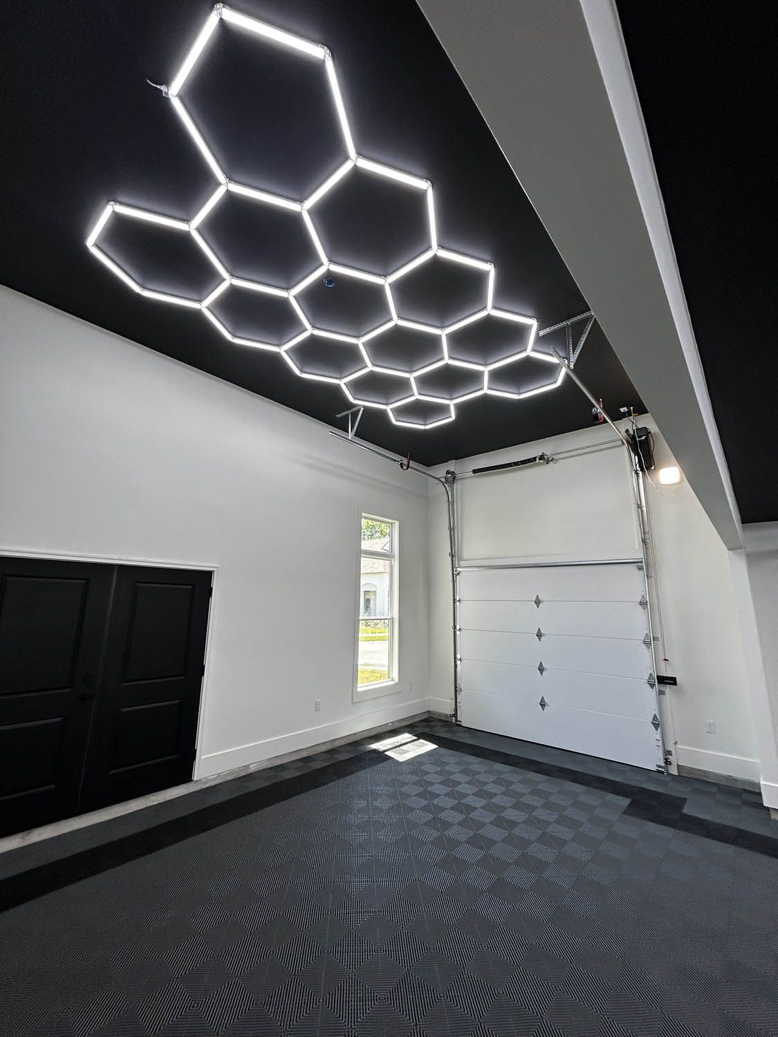 Modern garage interior with black ceiling and honeycomb LED lights. White walls, black door, and garage door.