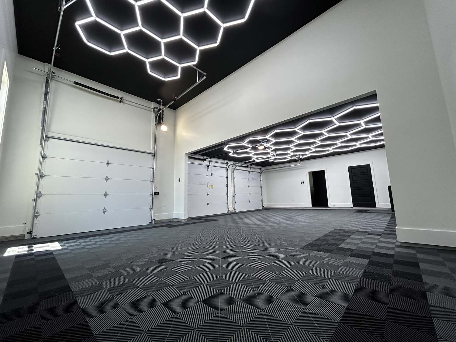 Spacious, empty room with geometric ceiling lights and garage doors; black and white patterned flooring.