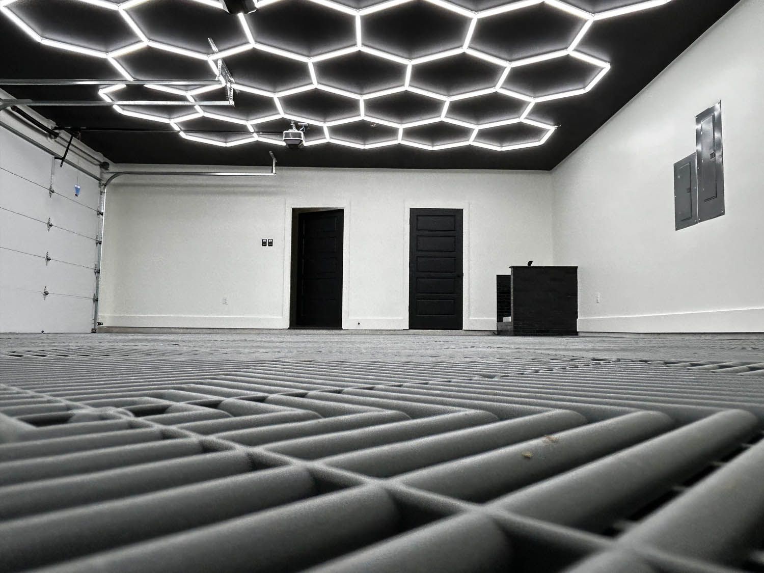 Garage interior with a honeycomb ceiling light fixture, two doors, and a black desk.