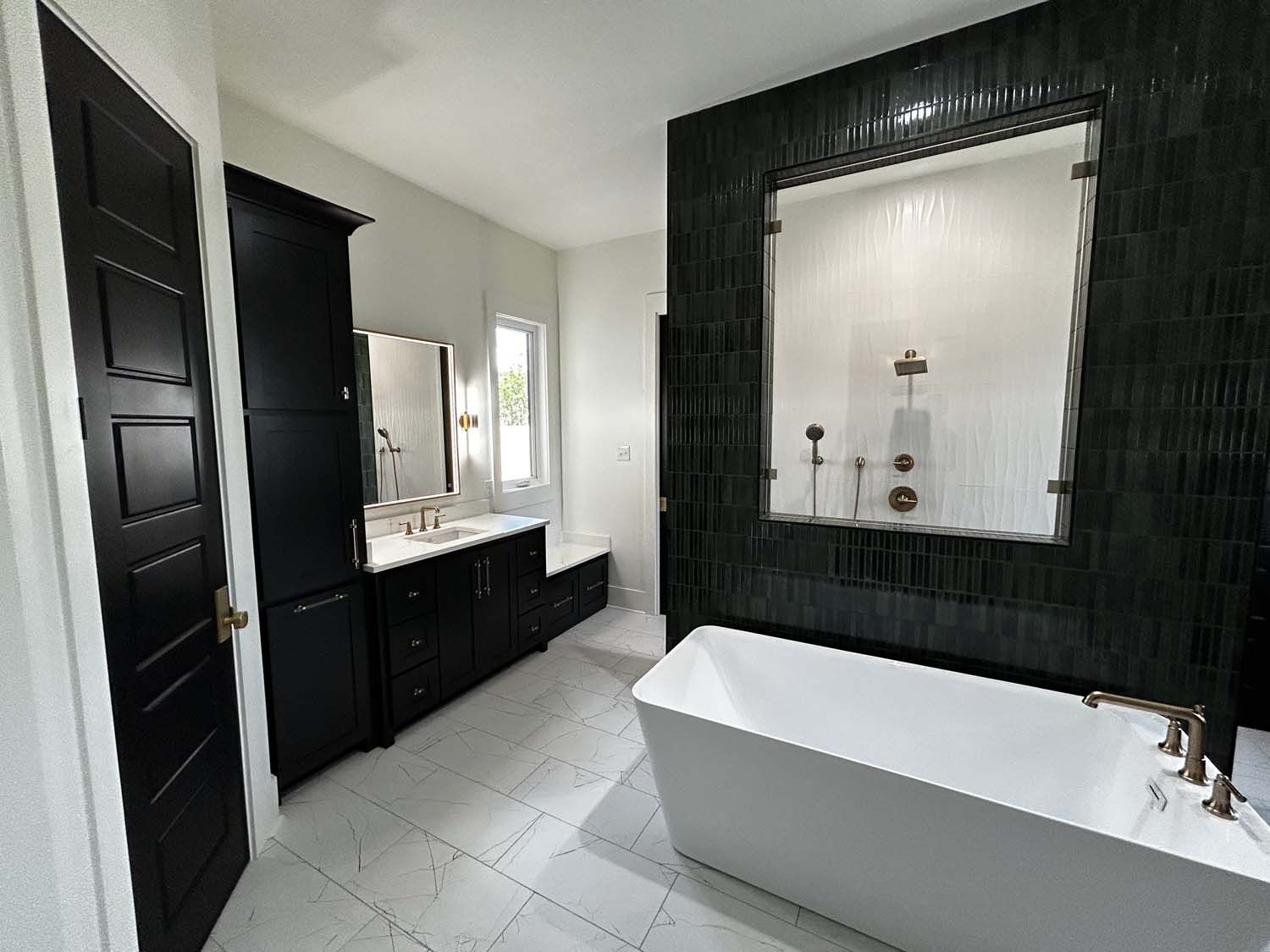 Modern bathroom with black accents, white tub and tile, dark tile feature wall, and tall cabinet.