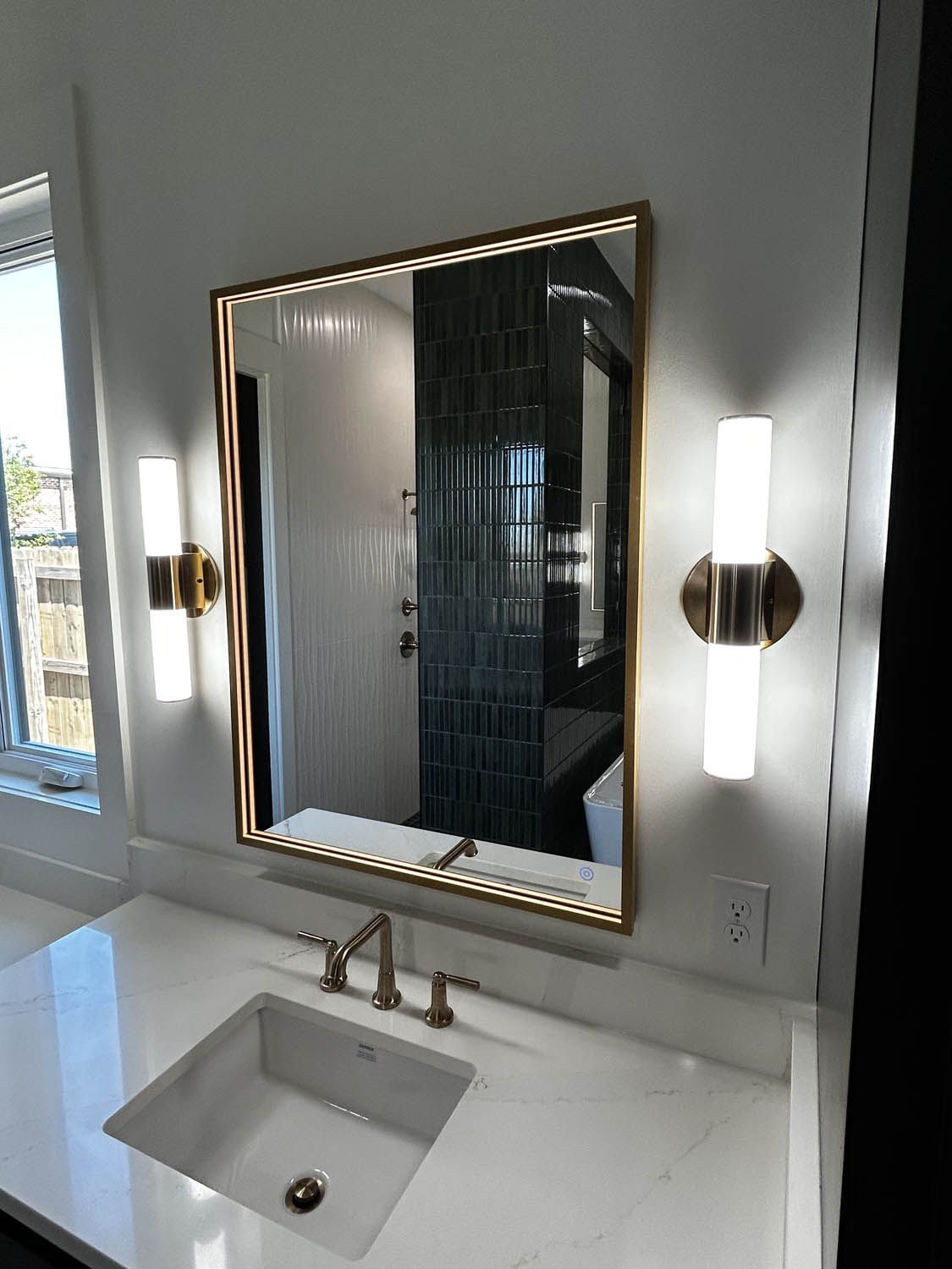 Bathroom with gold-framed mirror, two sconces, white countertop, and rectangular sink.