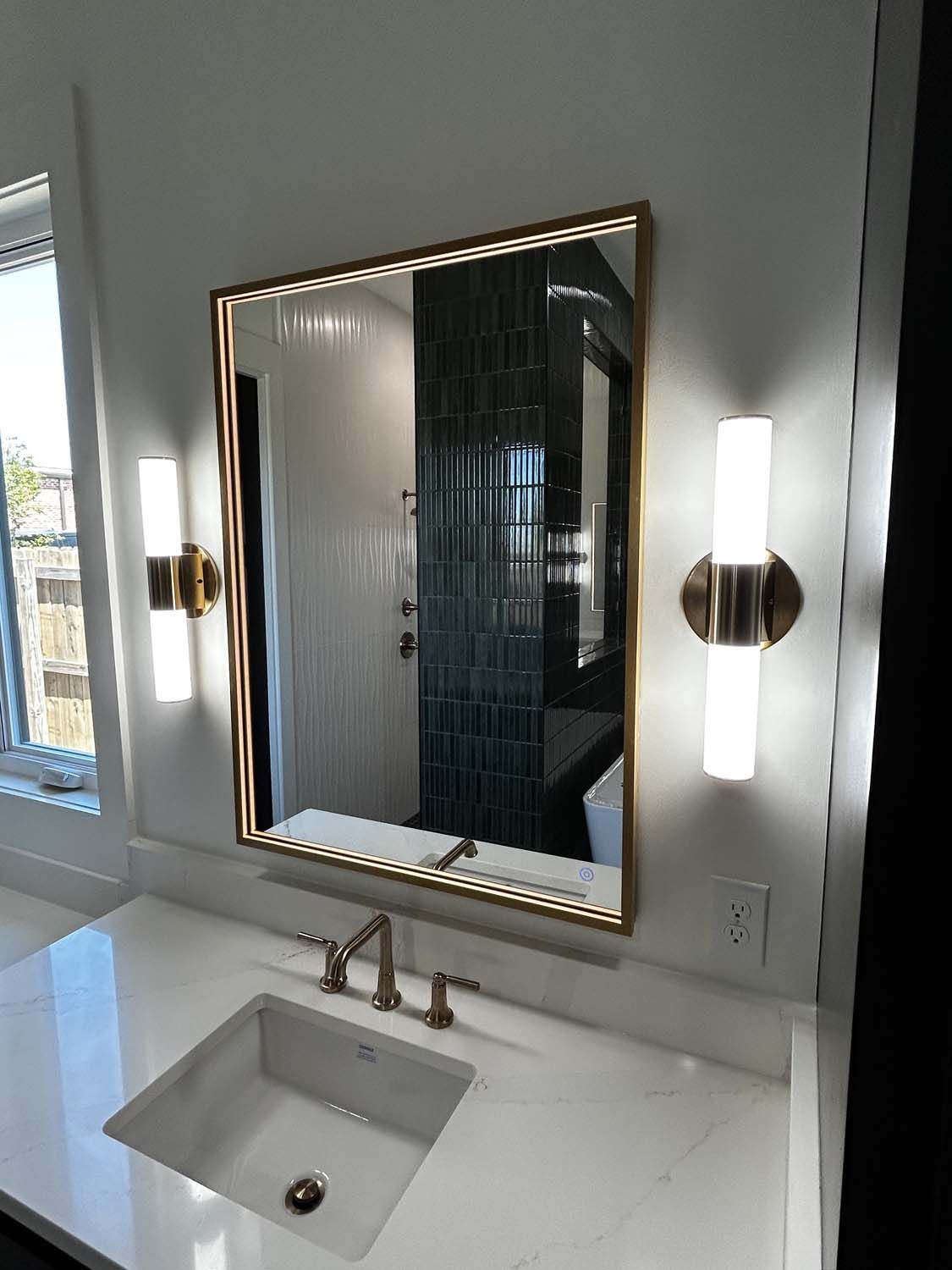 Bathroom with gold-framed mirror, two sconces, white countertop, and rectangular sink.