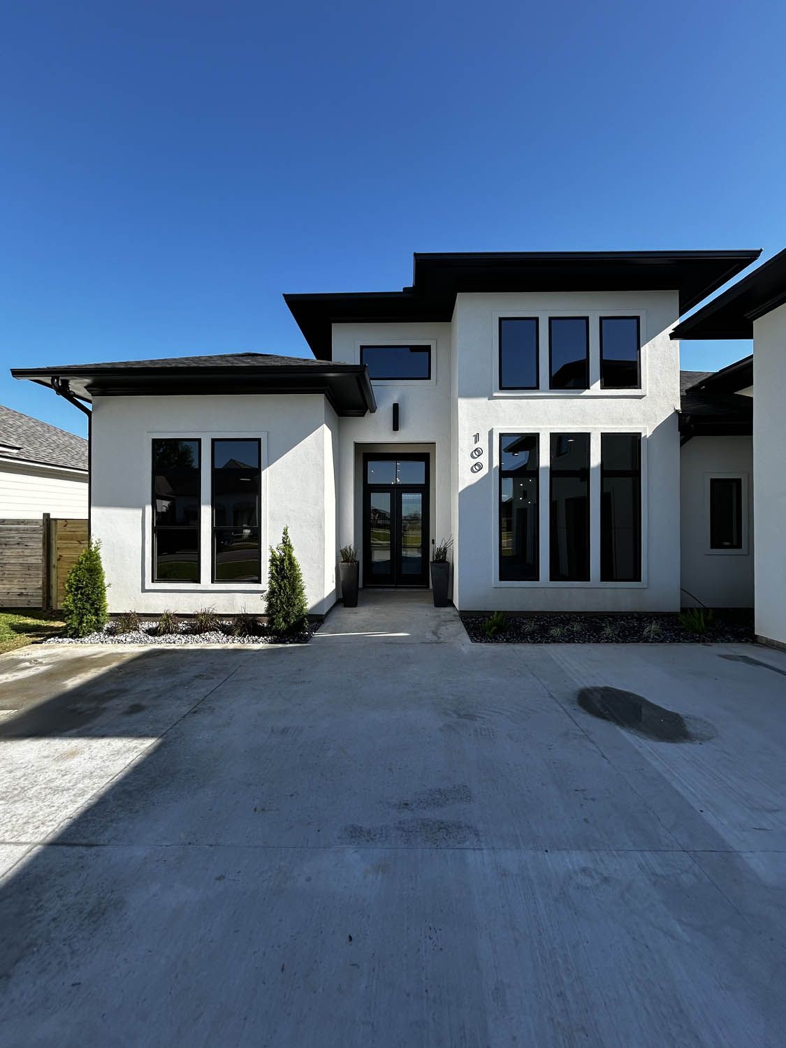 Modern white house with dark trim and large windows, driveway in front.