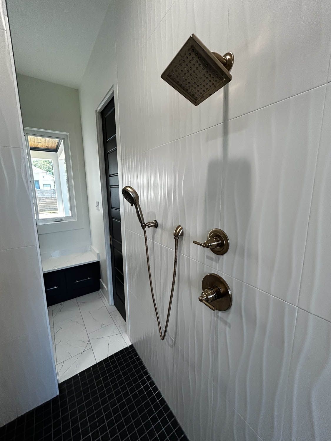 Modern bathroom shower with textured white tile and bronze fixtures.