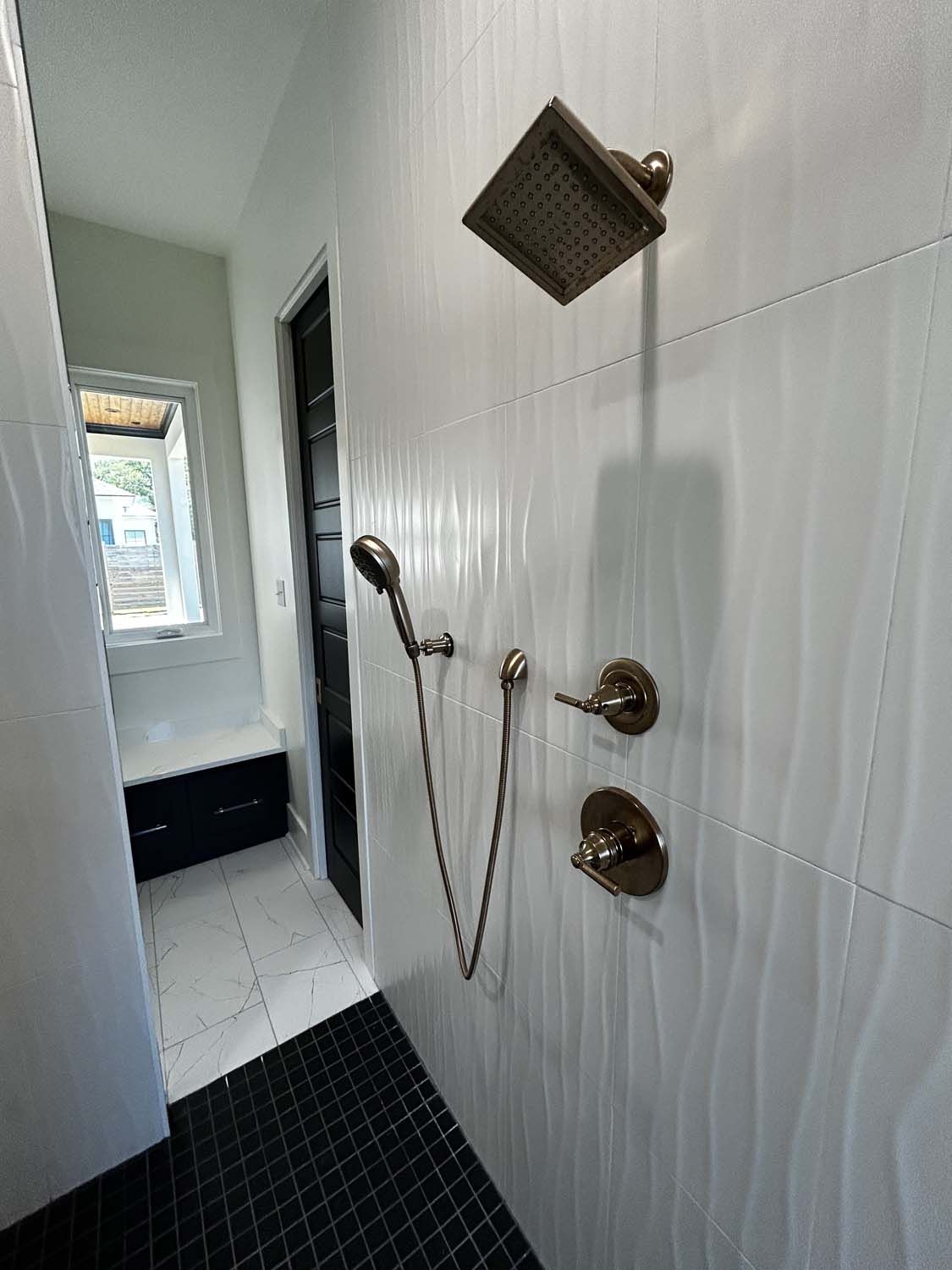 Modern shower with textured white wall tiles and bronze fixtures. Black tiled floor.