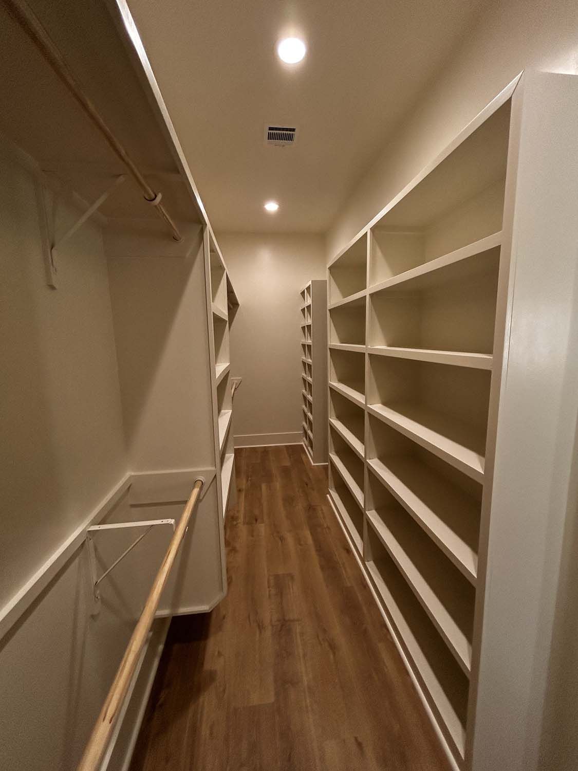 Long, narrow room with built-in white shelves and wooden floor. Empty.