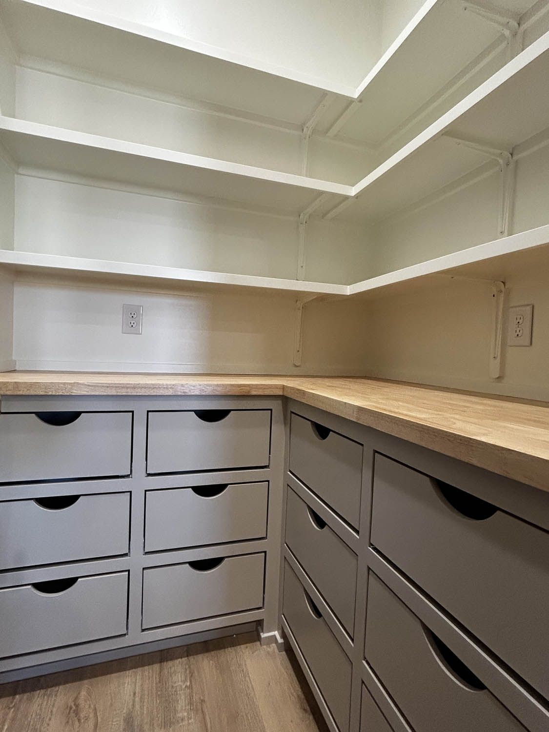 Corner pantry with light wood countertops, gray drawers, and white shelves.