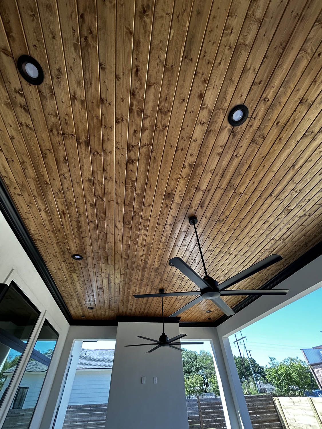 Wooden ceiling with recessed lights and two ceiling fans; outdoor patio.