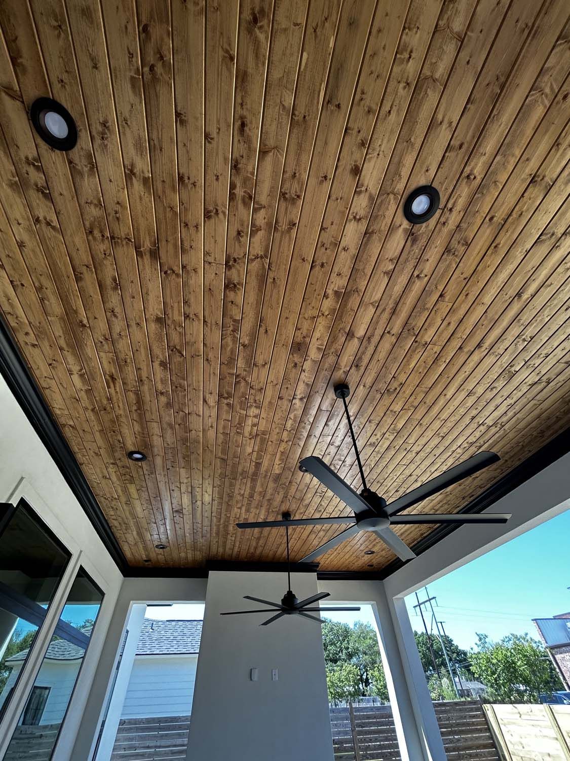 Wooden plank ceiling with two ceiling fans and recessed lights.