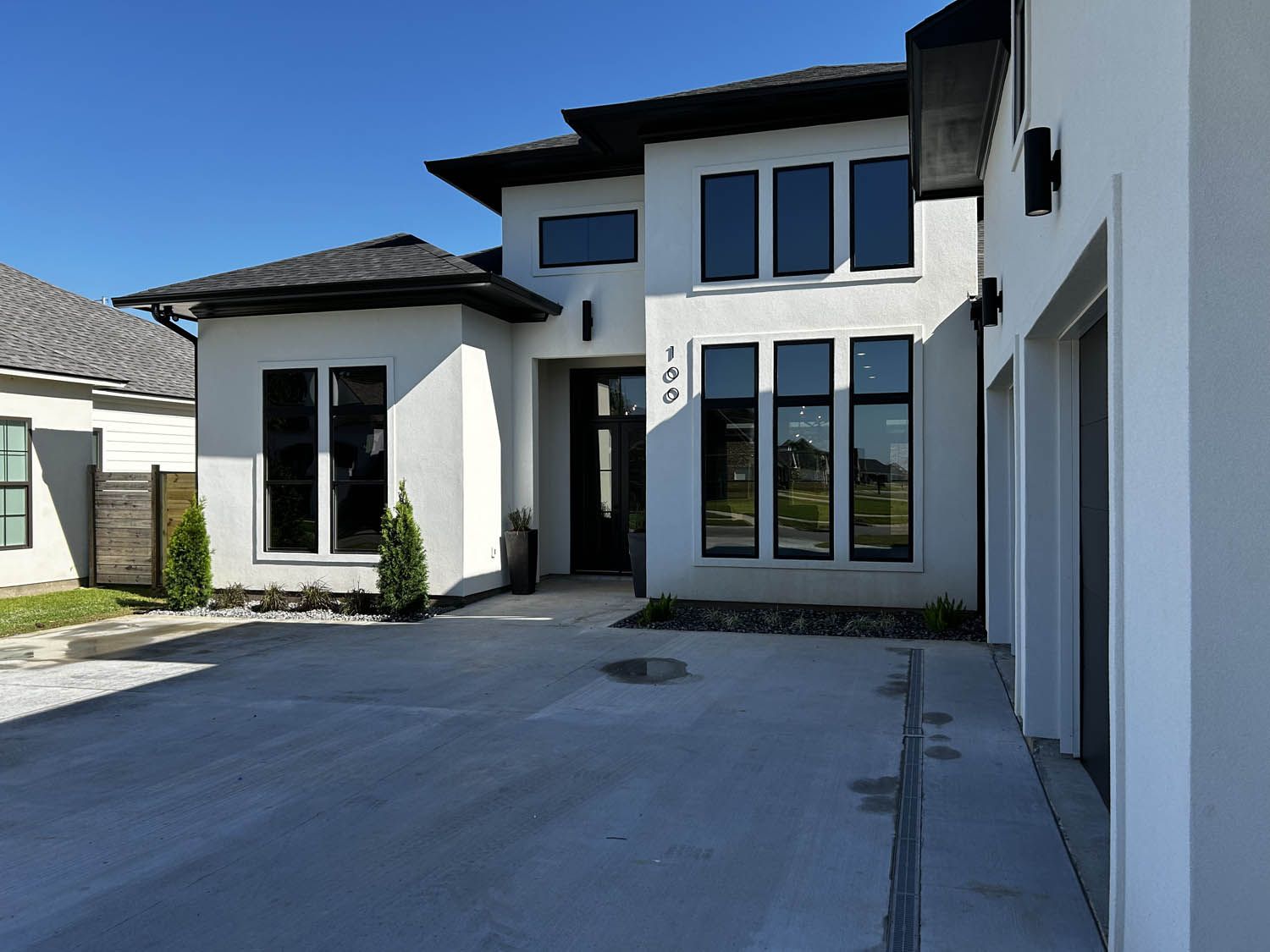Modern two-story house with white stucco walls, black windows, and a concrete driveway under a blue sky.
