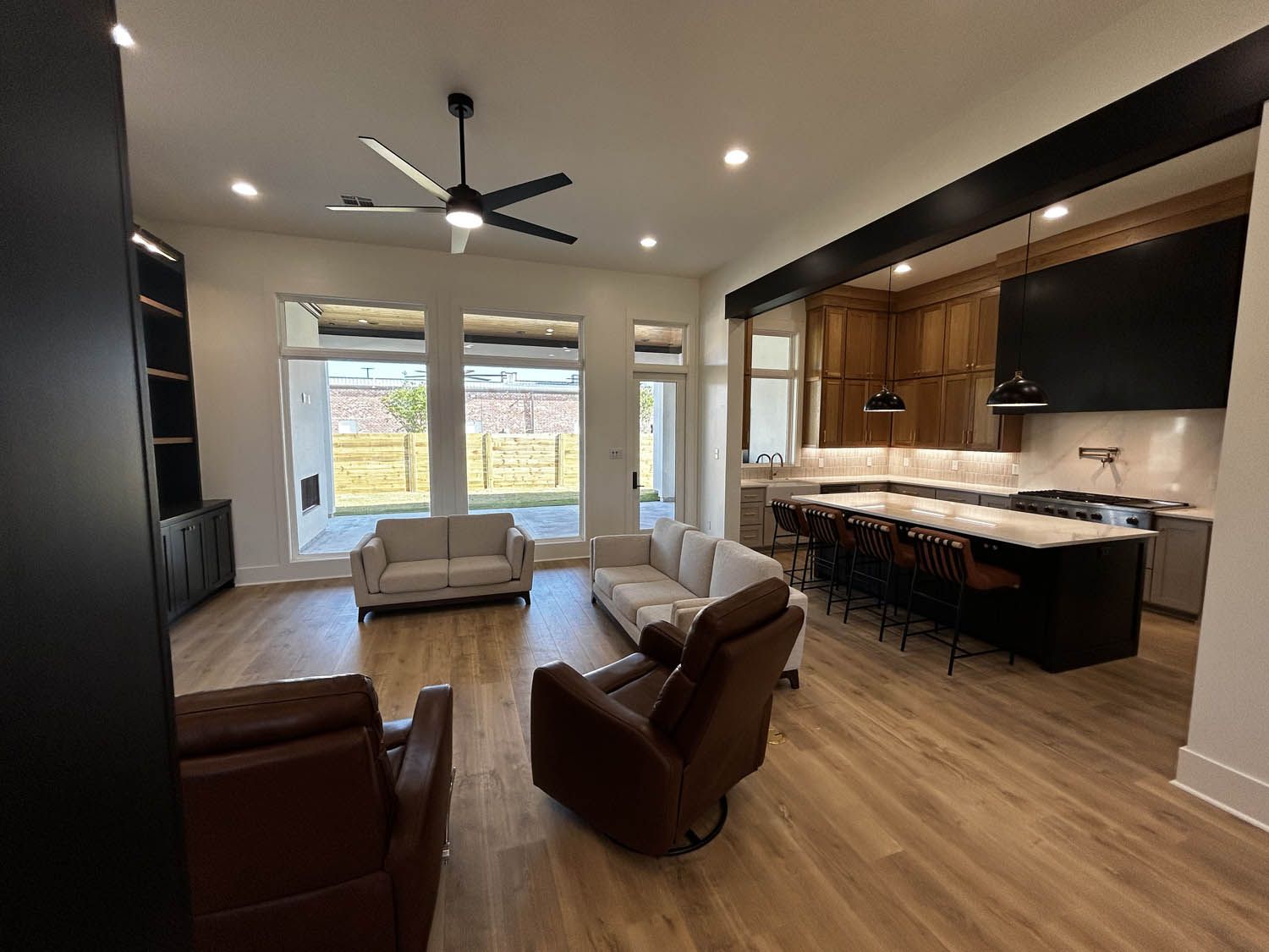 Open-concept living space with kitchen and seating areas. Light wood floors, white walls, and dark accents.