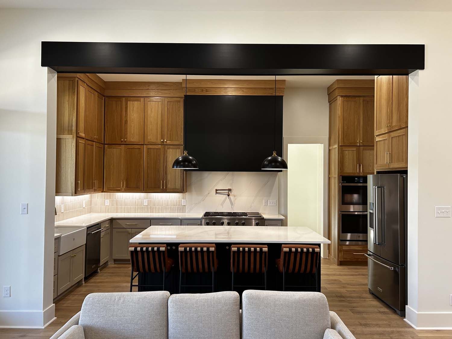Kitchen with wooden cabinets, gray island with seating, black hood, and stainless steel appliances.