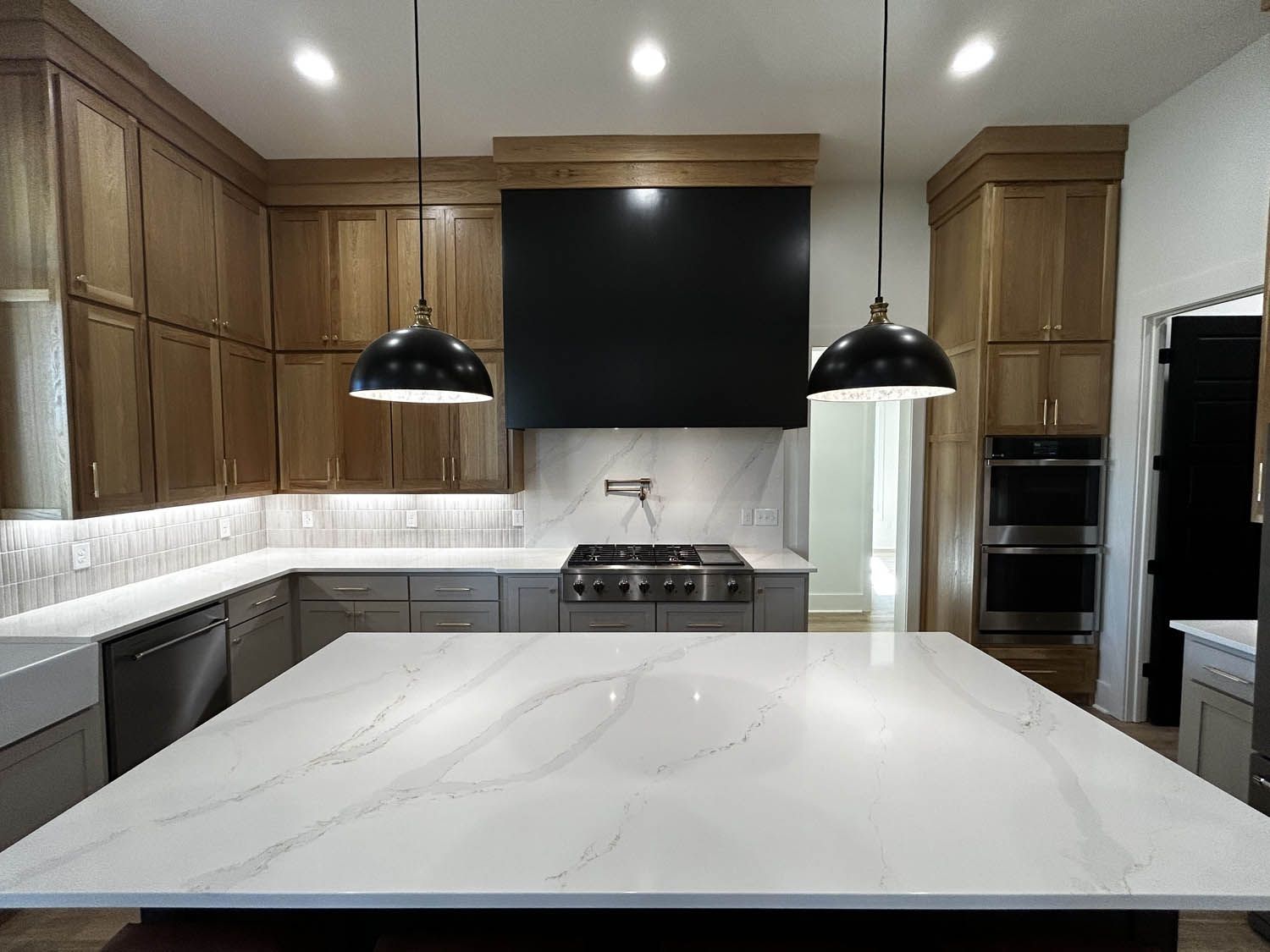 Modern kitchen with light oak cabinets, gray island, and two black pendant lights.