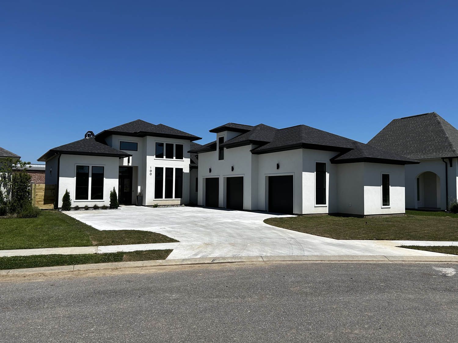 White modern house with black roof and driveway under a blue sky.