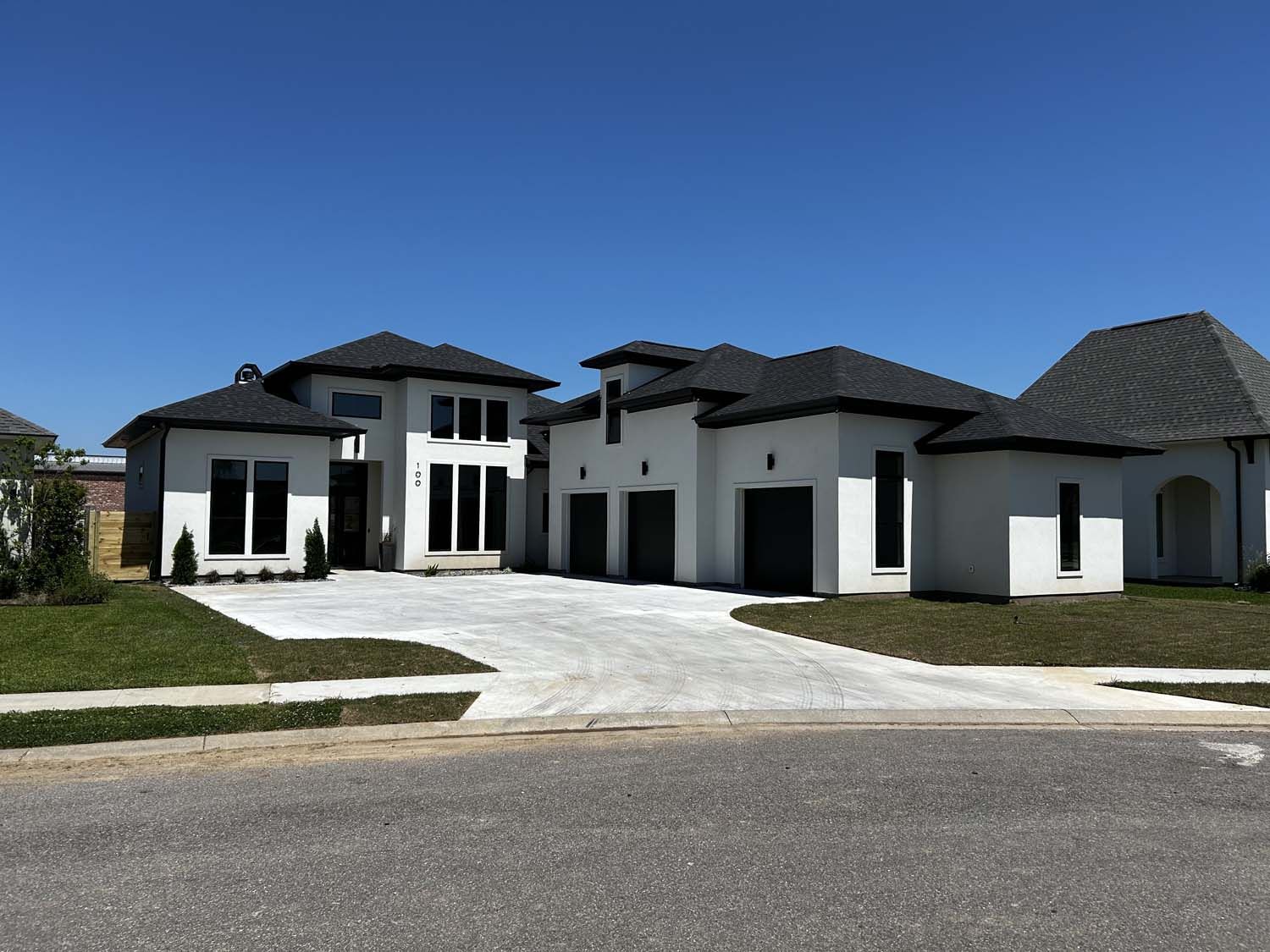 Modern white house with dark trim and driveway, blue sky.
