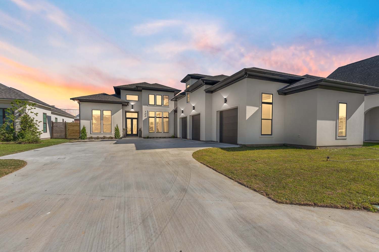 Modern home with a long driveway and three-car garage under a colorful sky at sunset.