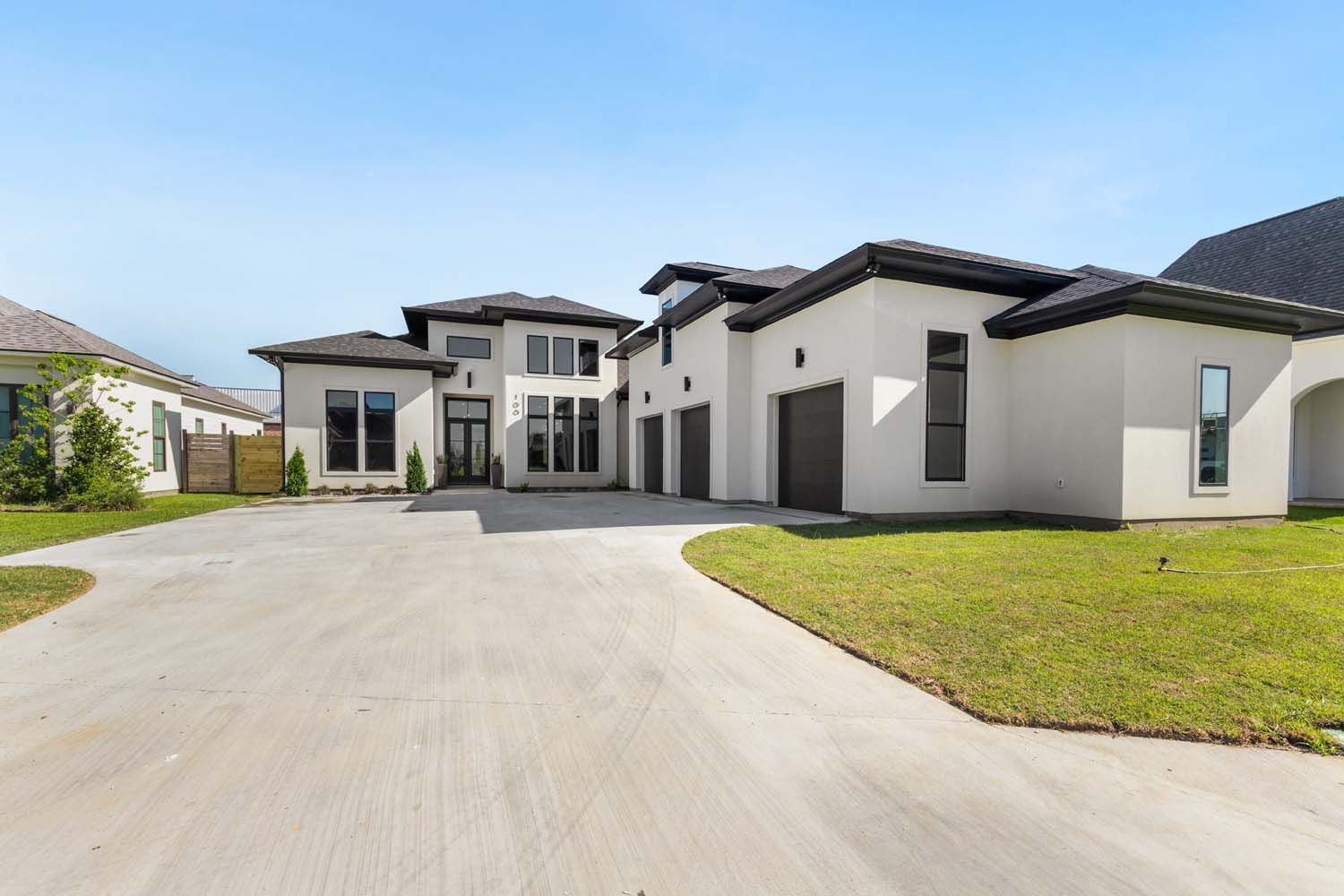 Modern, two-story house with a long driveway, three-car garage, and green lawn under a blue sky.