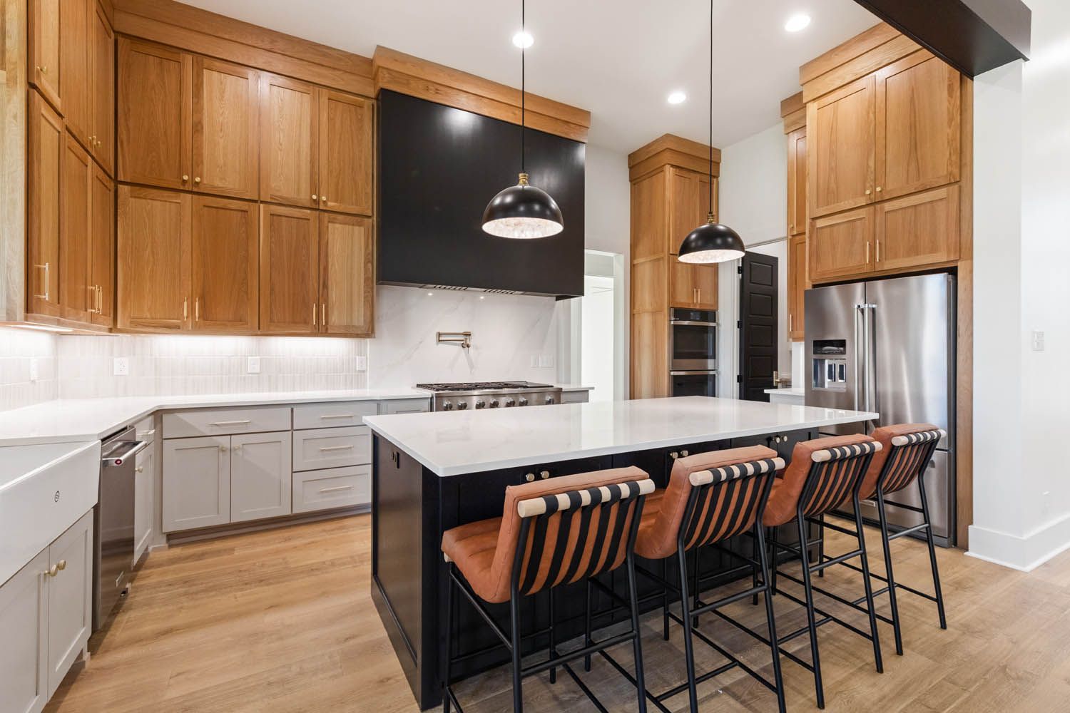 Modern kitchen with wood cabinets, black island, stainless steel appliances, and leather bar stools.