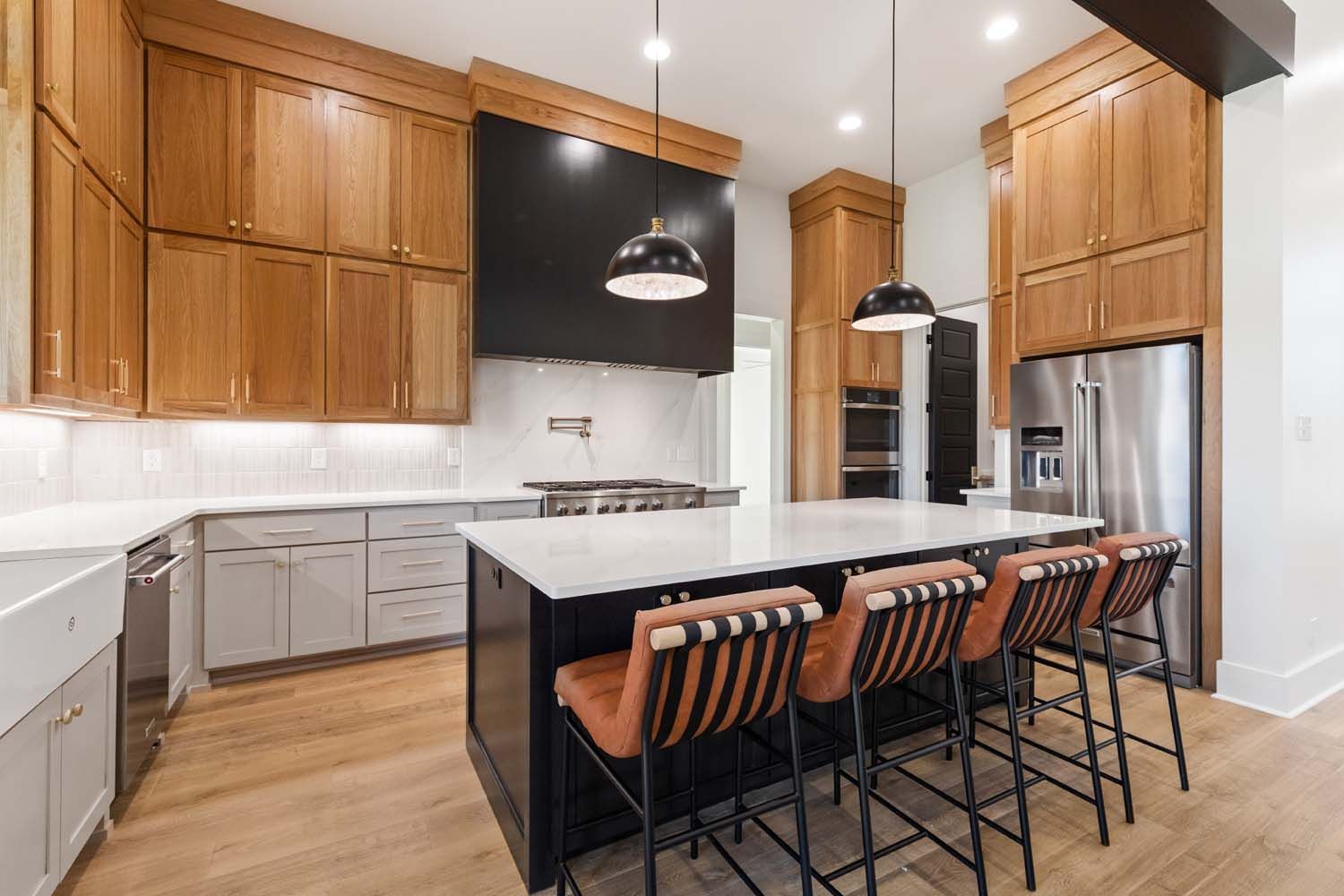 Modern kitchen with wood cabinets, black island, stainless steel appliances, and bar stools.