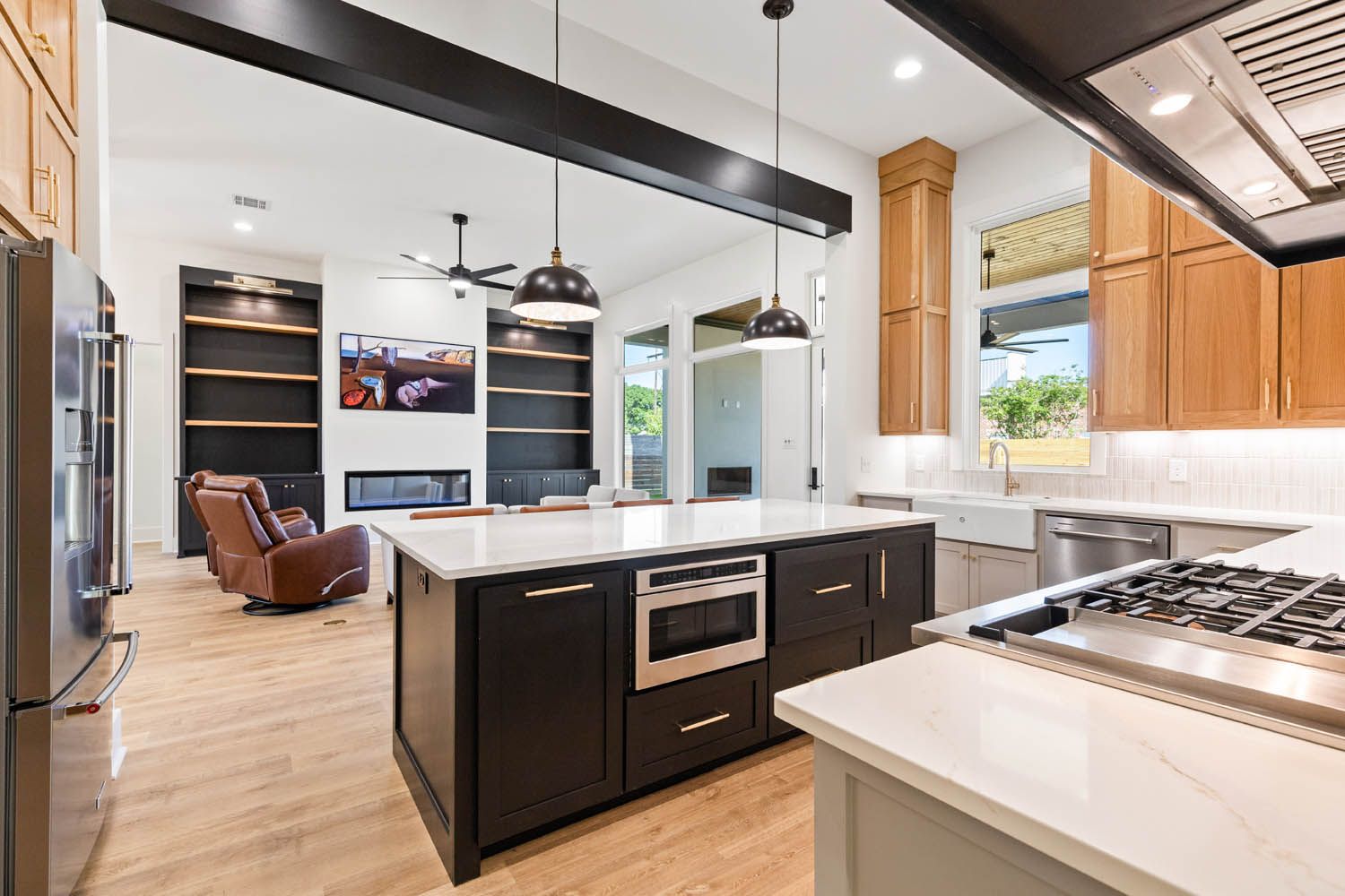 Modern kitchen with dark island, light countertops, and open view to living area with fireplace.