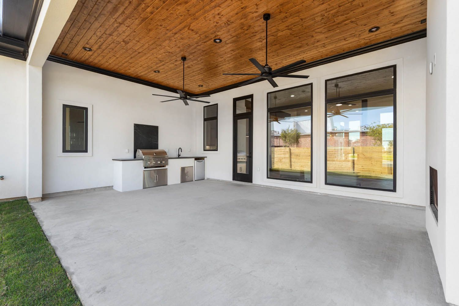Outdoor patio with concrete floor, built-in grill, wooden ceiling, and large windows.