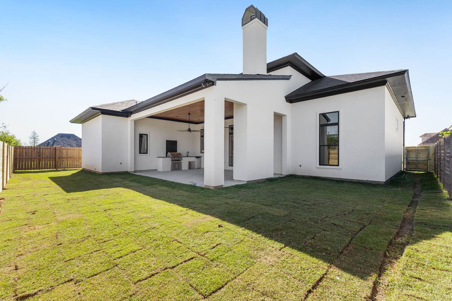White stucco house with outdoor kitchen, chimney, and new sod lawn.