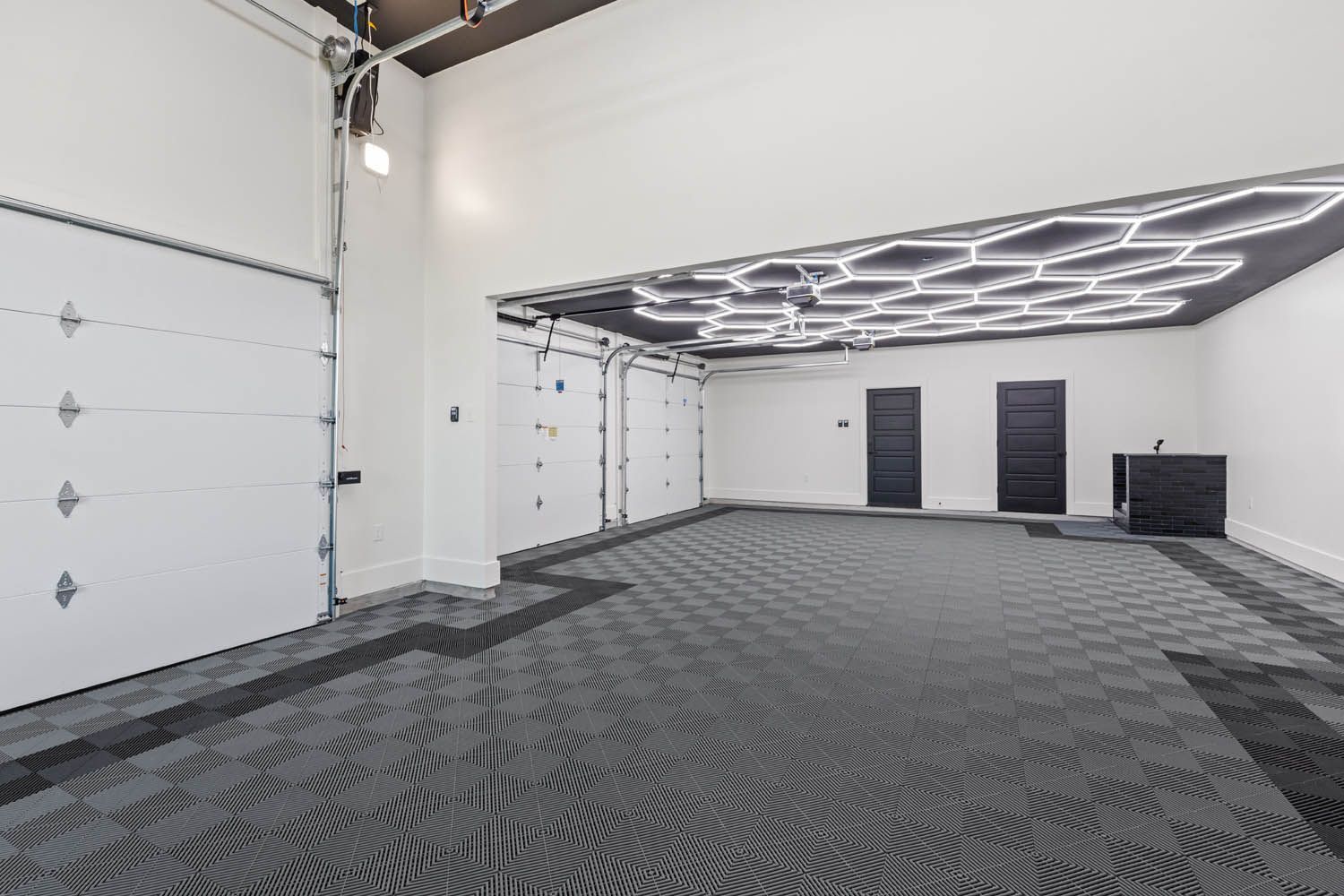 Spacious garage with patterned gray flooring, white garage doors, and a honeycomb-lit ceiling.