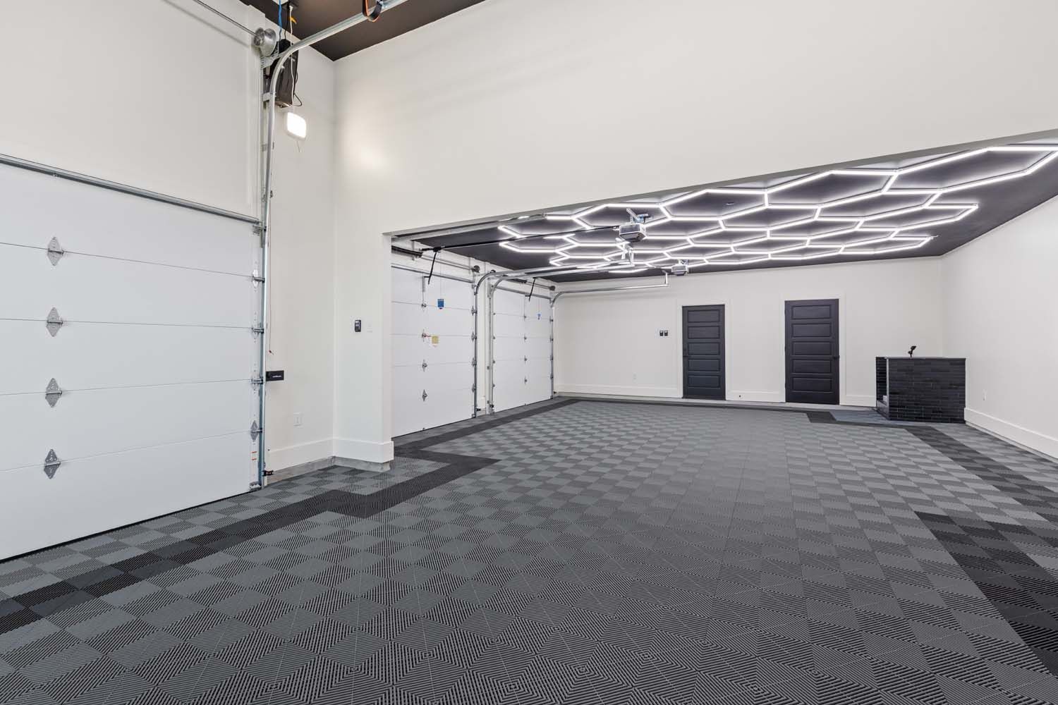 Spacious garage with patterned floor, white doors, and geometric ceiling lights.
