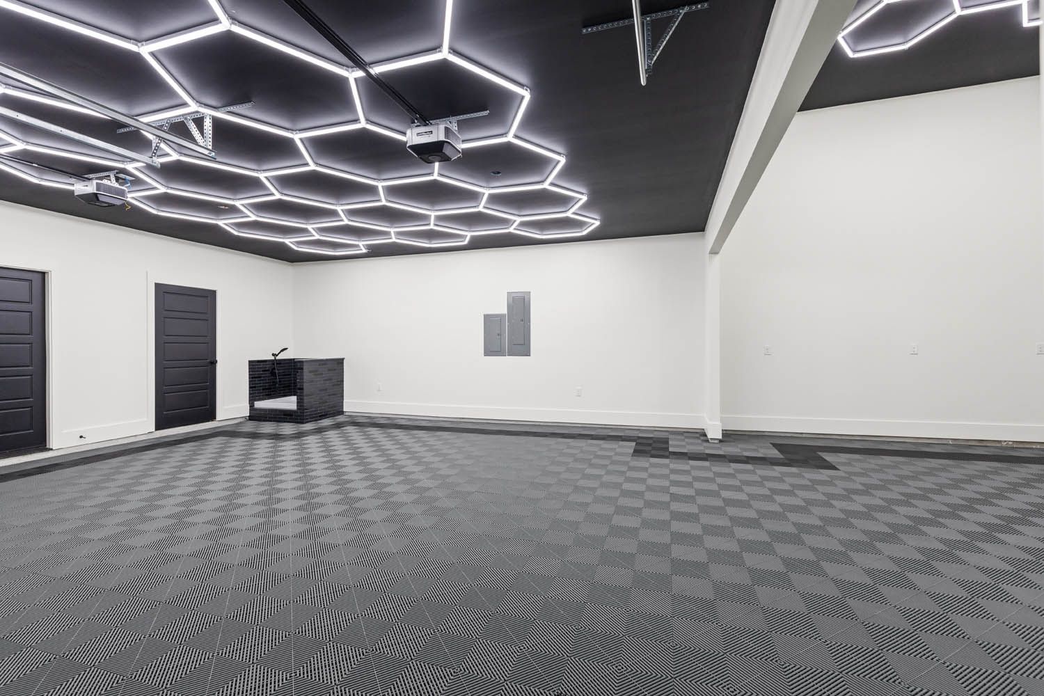 Empty room with hexagonal ceiling lights, dark floor tiles, and black doors.