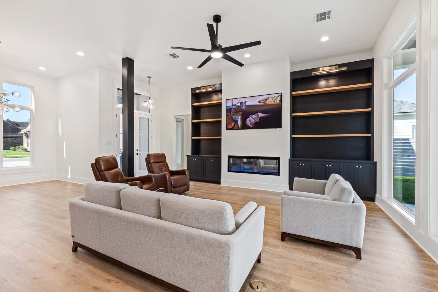 Spacious living room with neutral colors, built-ins, fireplace, light wood floors, and ceiling fan.