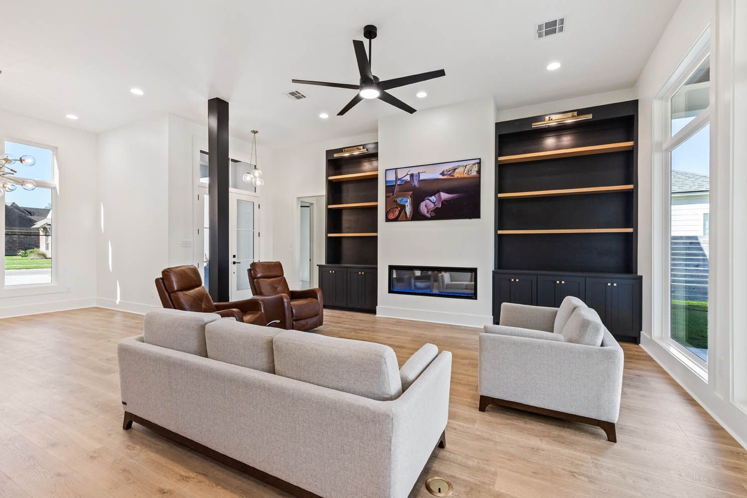 Spacious living room with white walls, built-in black bookshelves, fireplace, and light wood flooring.