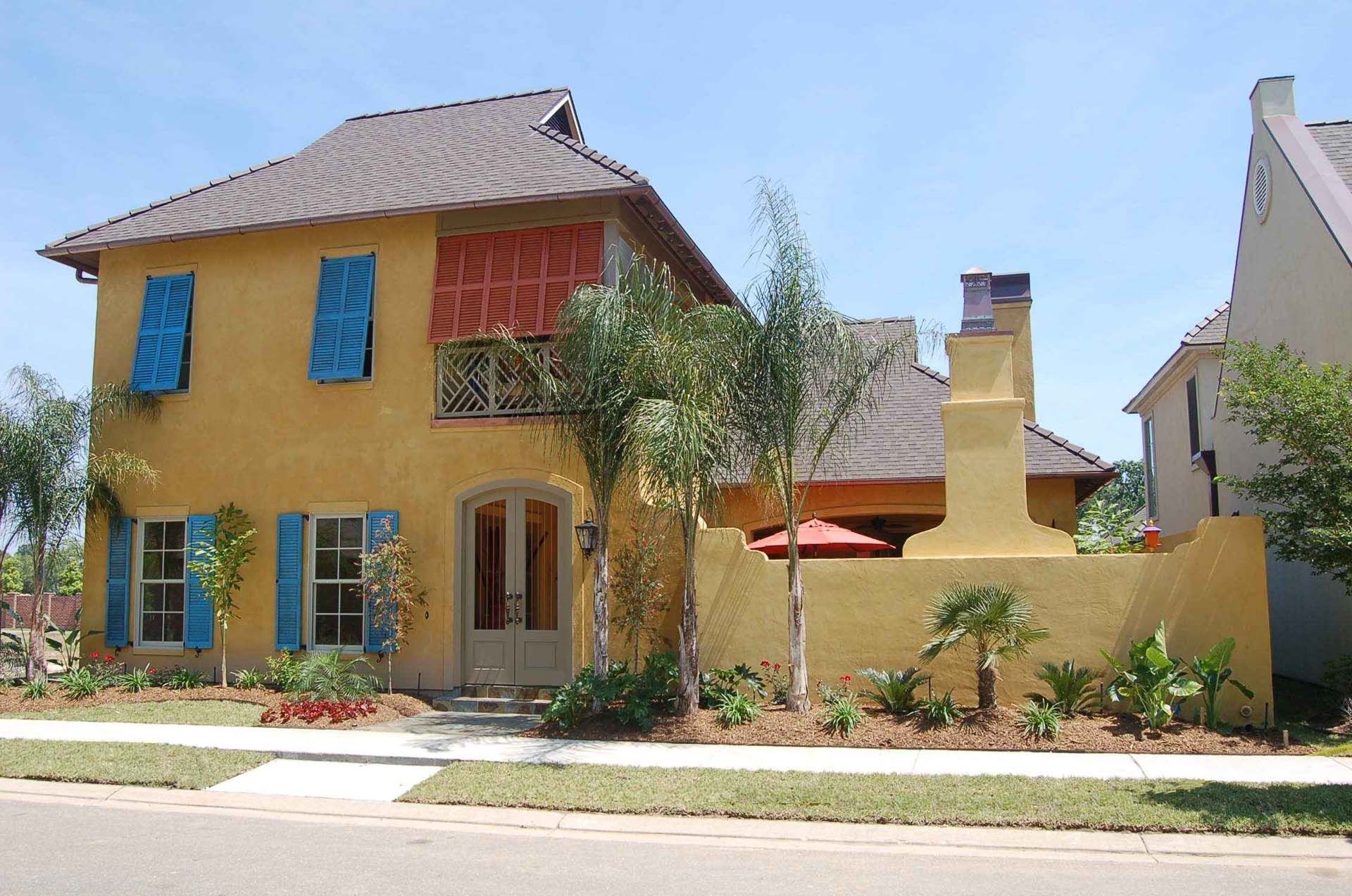 Yellow stucco house with blue shutters, red awnings, and a brick chimney.