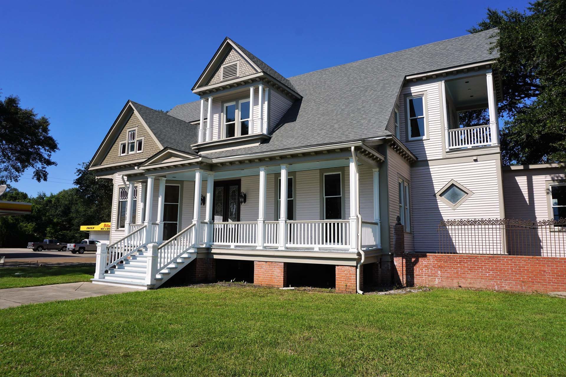 Two-story white house with porch, dormers, and gray roof, in front of green lawn on a sunny day.