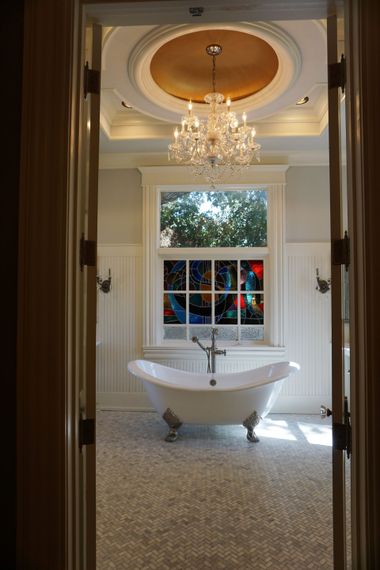 Luxurious bathroom with clawfoot tub, stained glass window, chandelier, and mosaic tile floor.