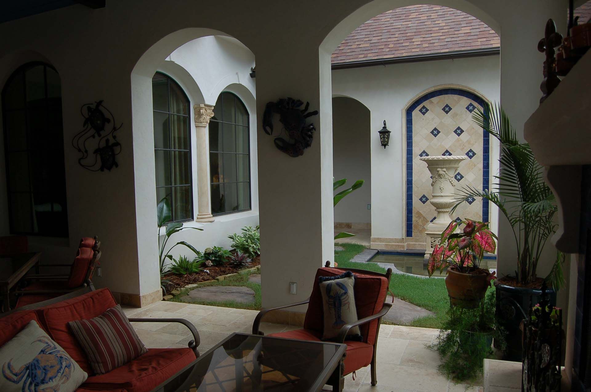 Patio with arched doorways, red furniture, fountain, and tiled wall.