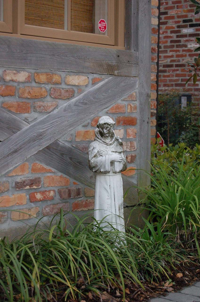 Stone statue of a monk in a garden, with brick and wood building background.