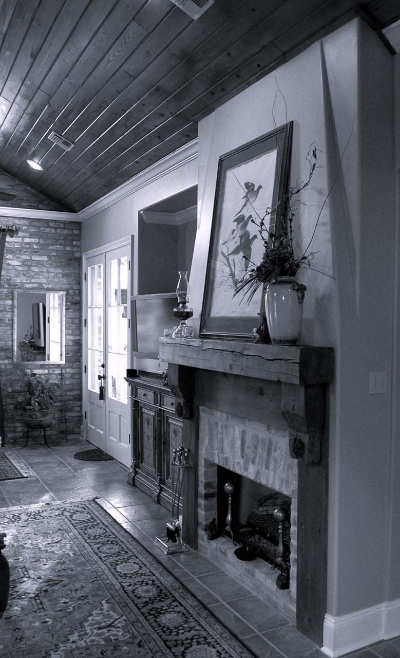 Fireplace in a room with brick wall, wooden ceiling, and a rug. Painting and vase are on the mantel.