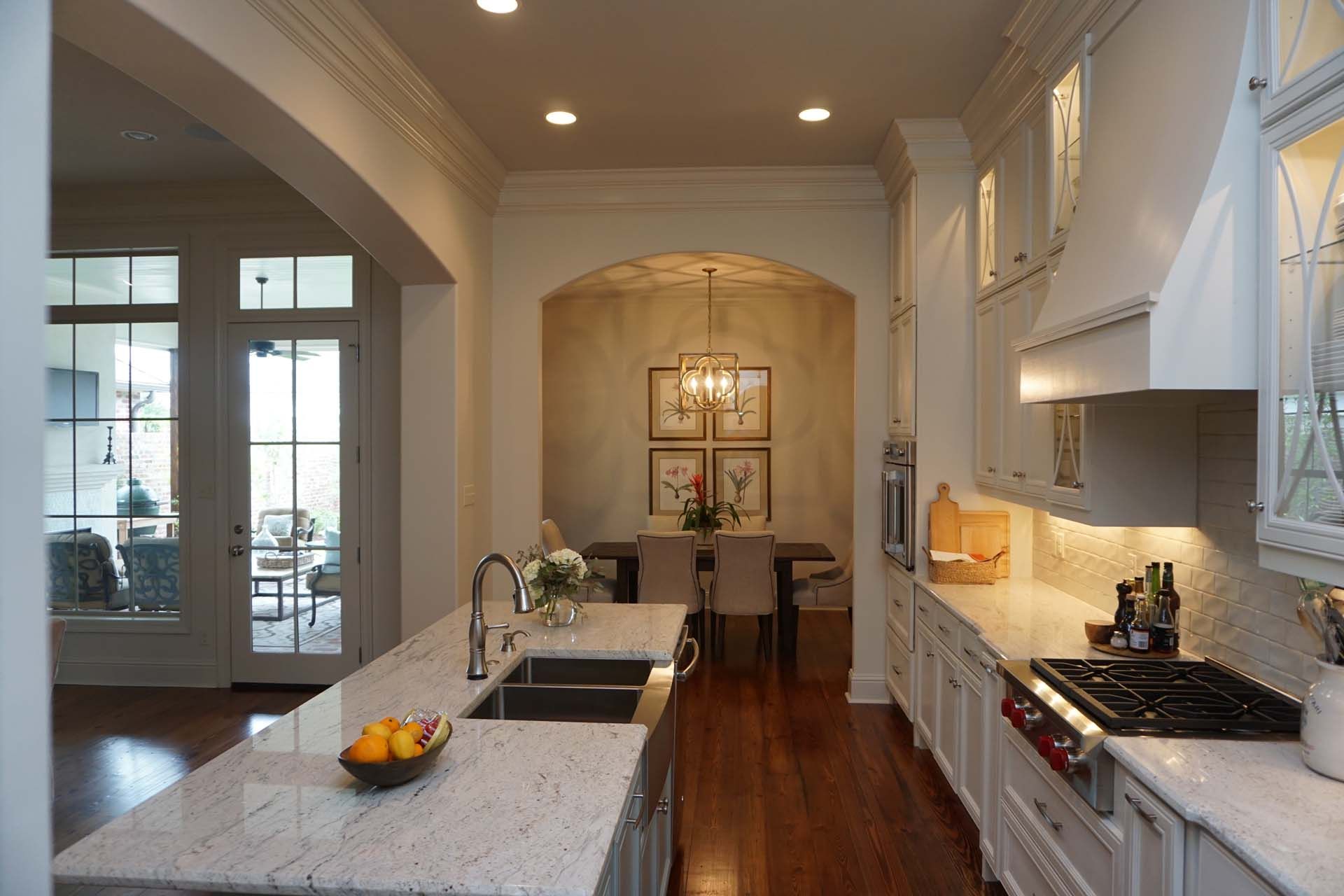 Elegant white kitchen with granite countertops, archway to dining area, hardwood floors.