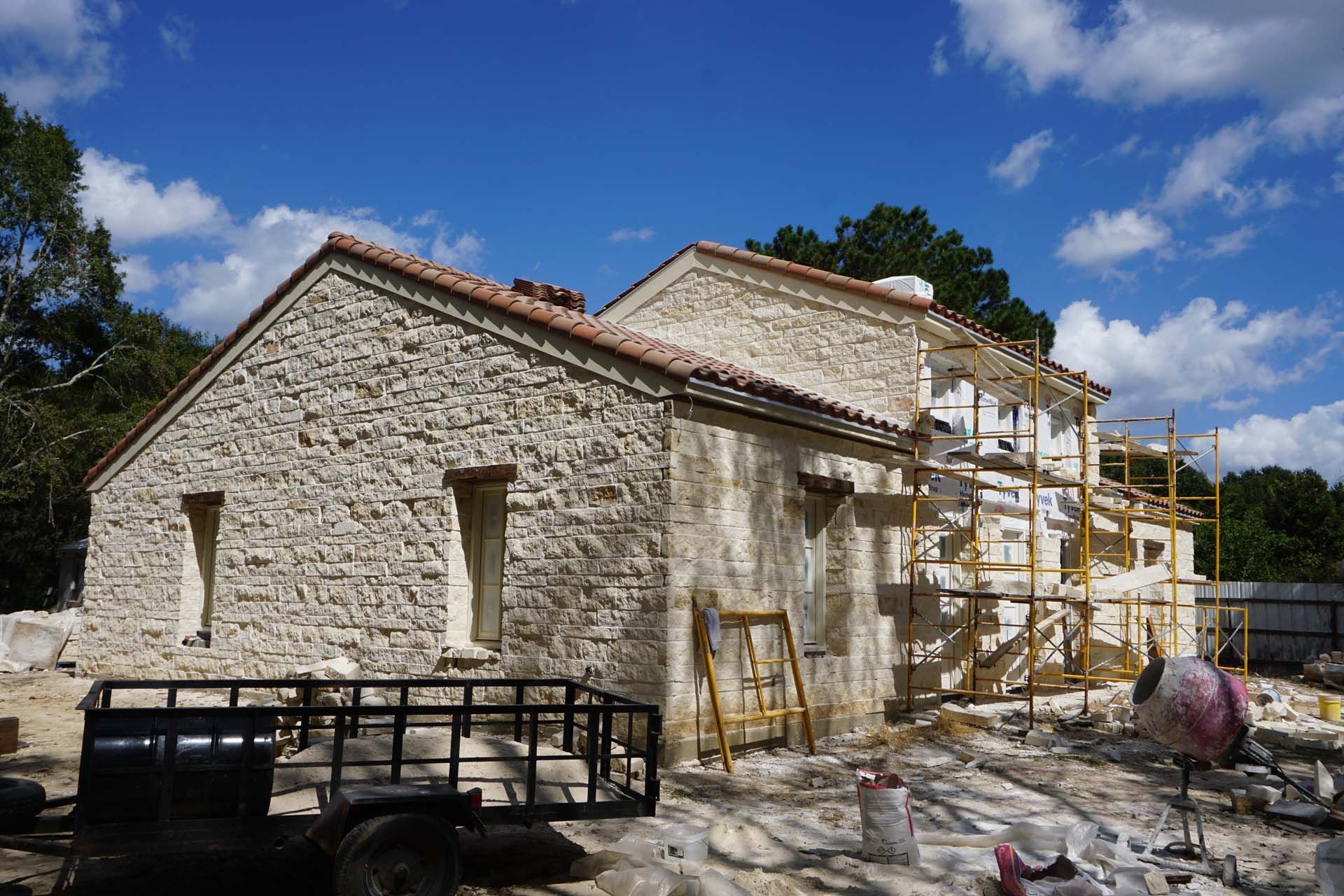 Stone building under construction with scaffolding, trailer, and blue sky.