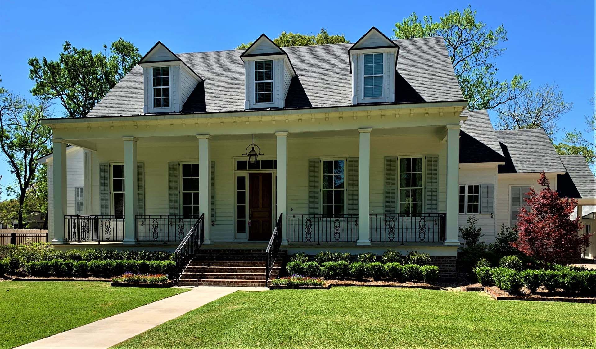 White house with columns, a porch, and a gray roof on a sunny day.