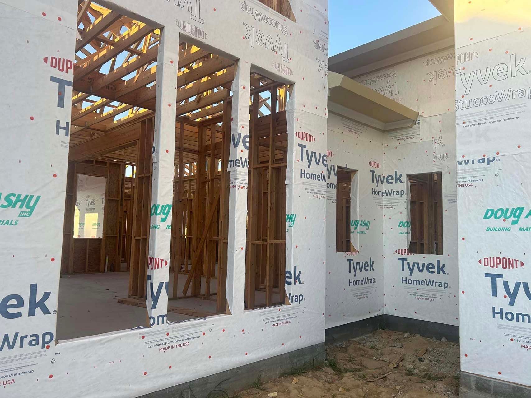 Exterior view of a house under construction; wooden frame and Tyvek house wrap visible.